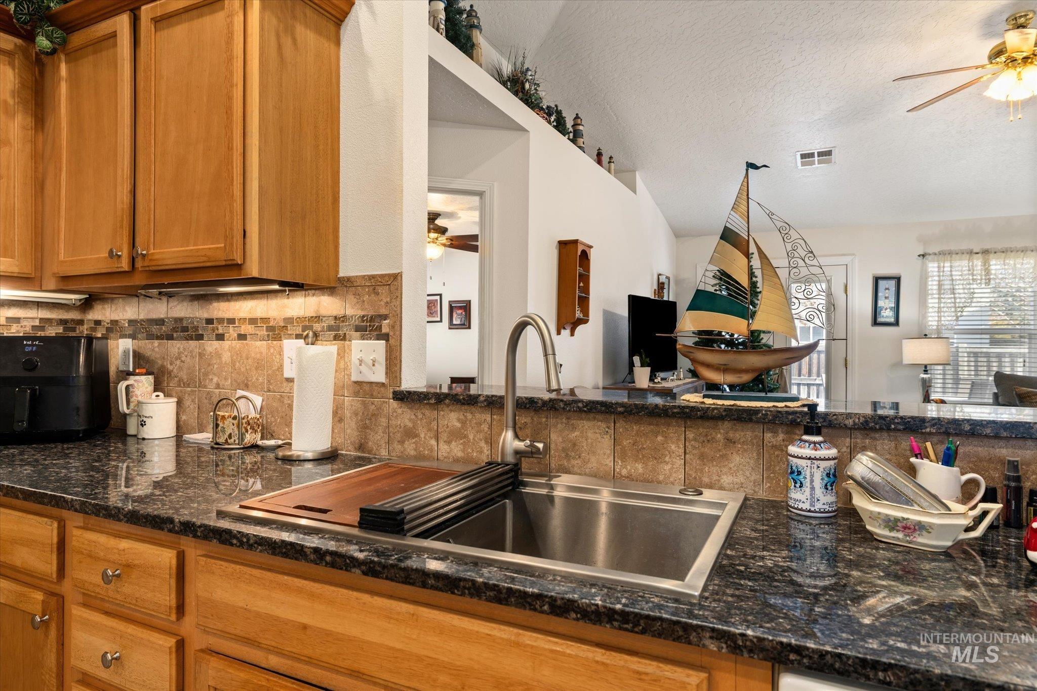 Kitchen with a ceiling fan, open floor plan, brown cabinetry, backsplash, and a textured ceiling