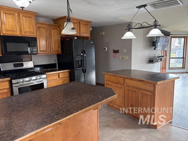 Kitchen featuring pendant lighting, brown cabinetry, black appliances, a center island, and dark countertops