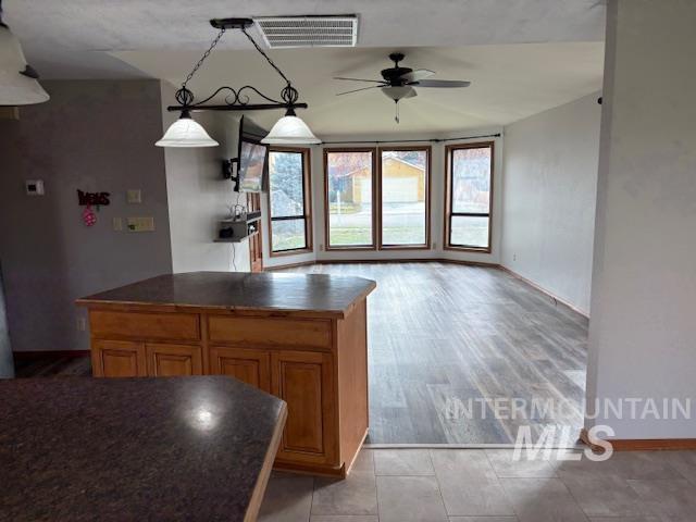 Kitchen featuring dark countertops, hanging light fixtures, brown cabinetry, open floor plan, and ceiling fan