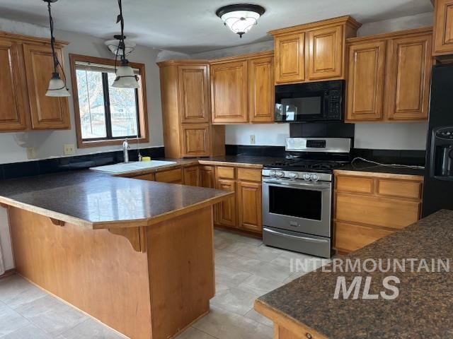 Kitchen with brown cabinetry, dark countertops, black appliances, and hanging light fixtures