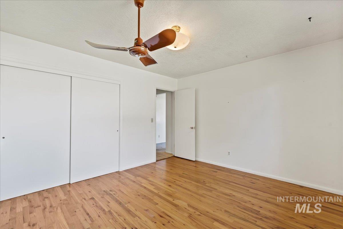 Unfurnished bedroom featuring a textured ceiling, a closet, light wood finished floors, and ceiling fan