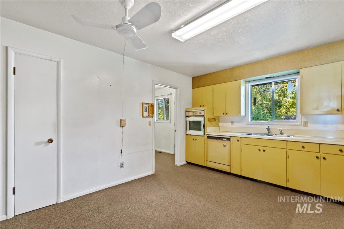 Kitchen featuring light countertops, dishwasher, oven, light colored carpet, and a textured ceiling