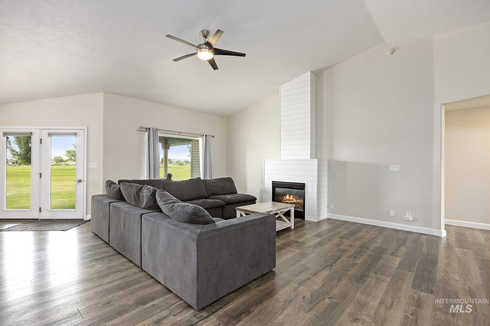 Living area featuring vaulted ceiling, dark wood-type flooring, a fireplace, and a ceiling fan
