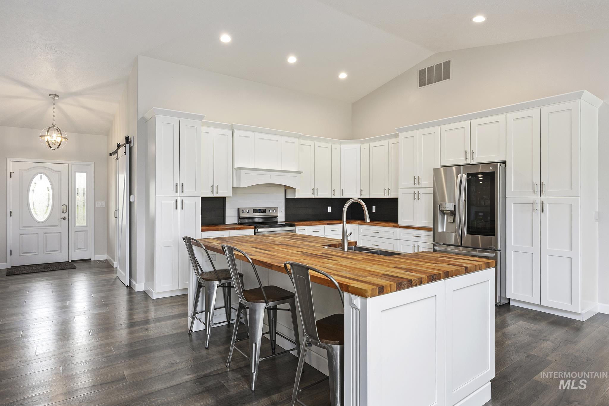 Kitchen with a barn door, white cabinets, appliances with stainless steel finishes, a kitchen island with sink, and a kitchen breakfast bar