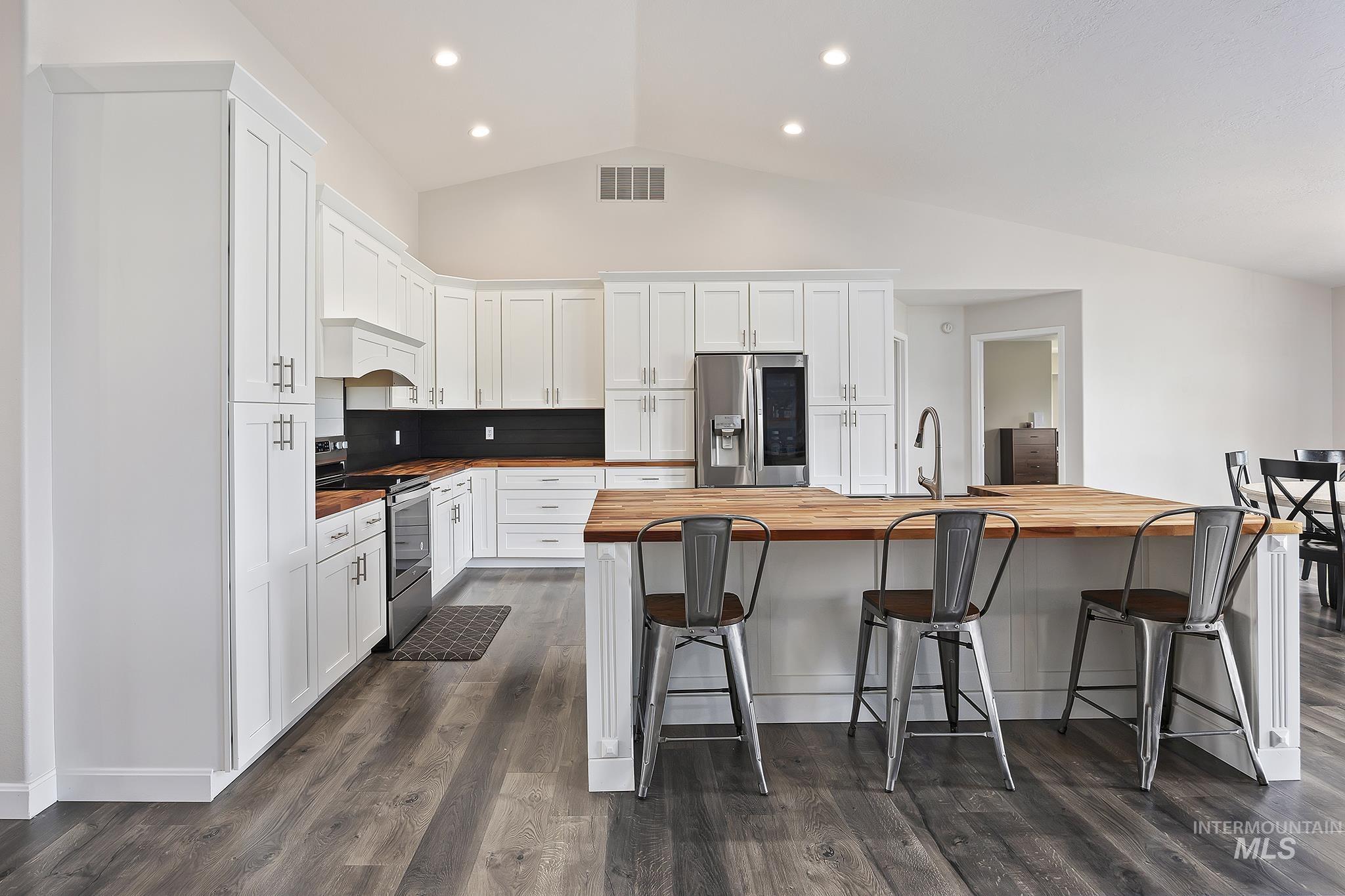 Kitchen featuring butcher block countertops, stainless steel appliances, white cabinetry, vaulted ceiling, and dark wood finished floors