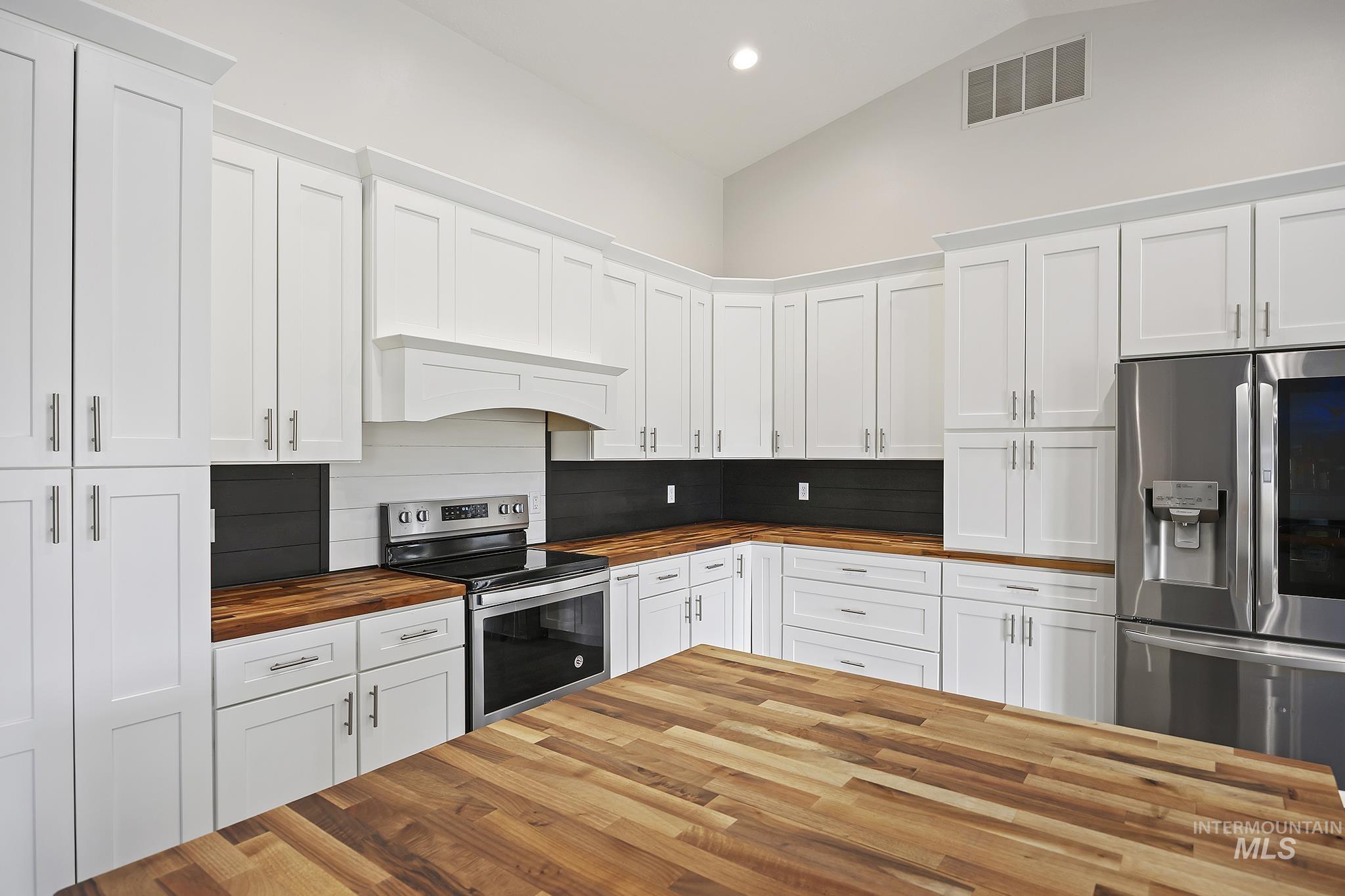 Kitchen featuring wood counters, white cabinets, appliances with stainless steel finishes, recessed lighting, and high vaulted ceiling