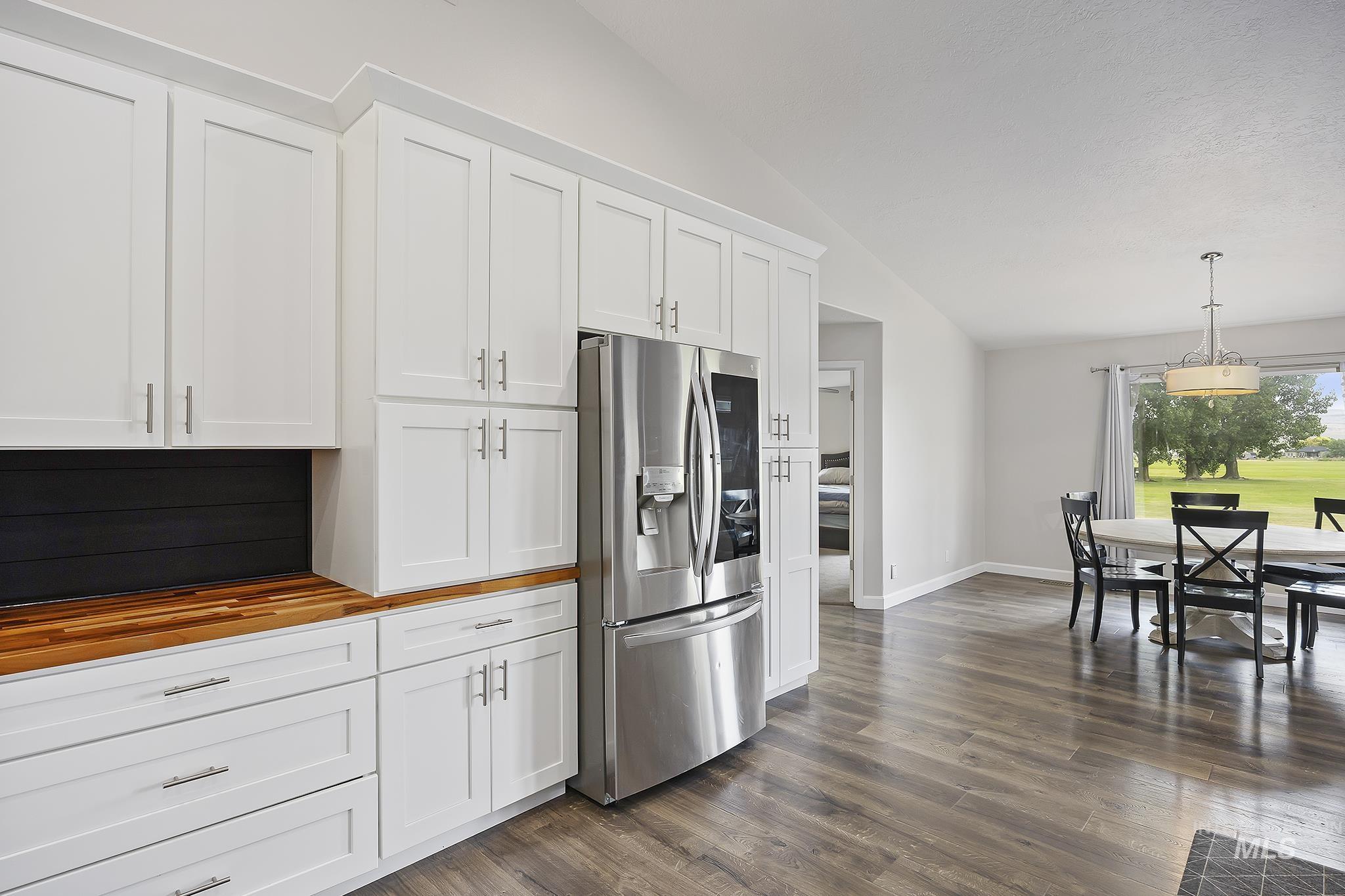 Kitchen featuring white cabinetry, stainless steel refrigerator with ice dispenser, lofted ceiling, butcher block countertops, and decorative light fixtures