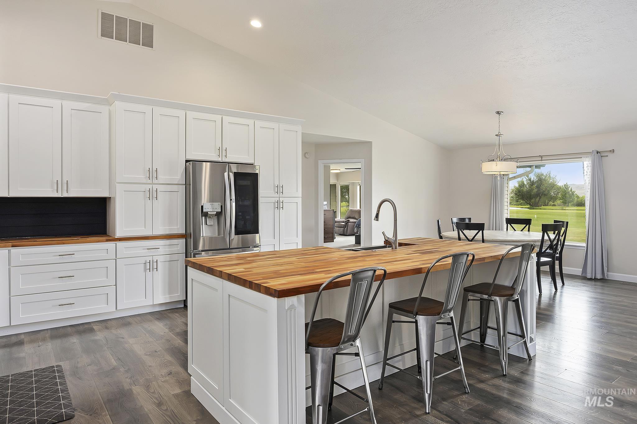 Kitchen with white cabinets, butcher block counters, stainless steel fridge, recessed lighting, and high vaulted ceiling