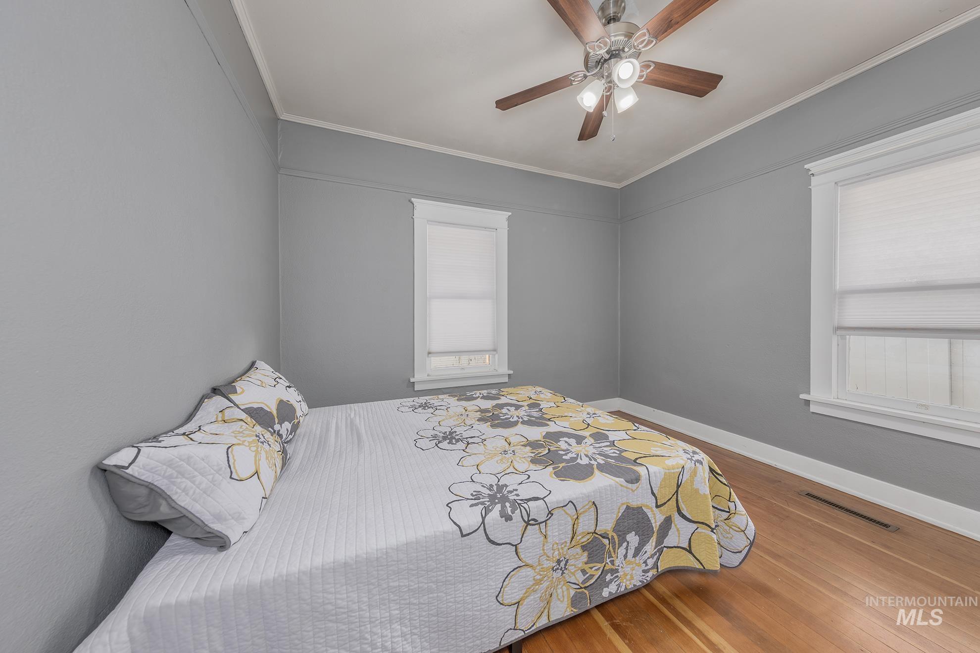 Bedroom featuring wood finished floors, ornamental molding, ceiling fan, and multiple windows