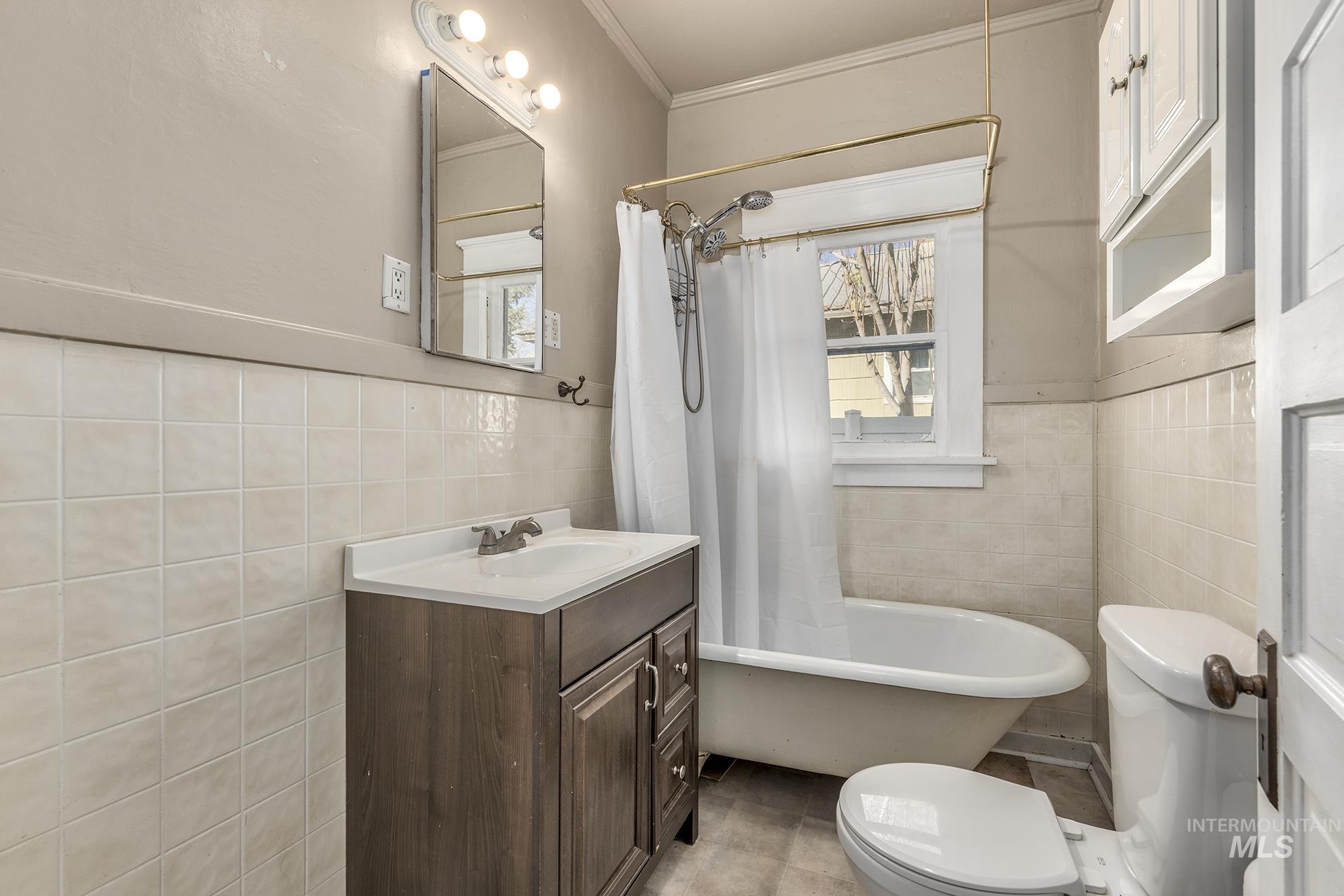 Bathroom with vanity, tile walls, shower / tub combo with curtain, crown molding, and wainscoting