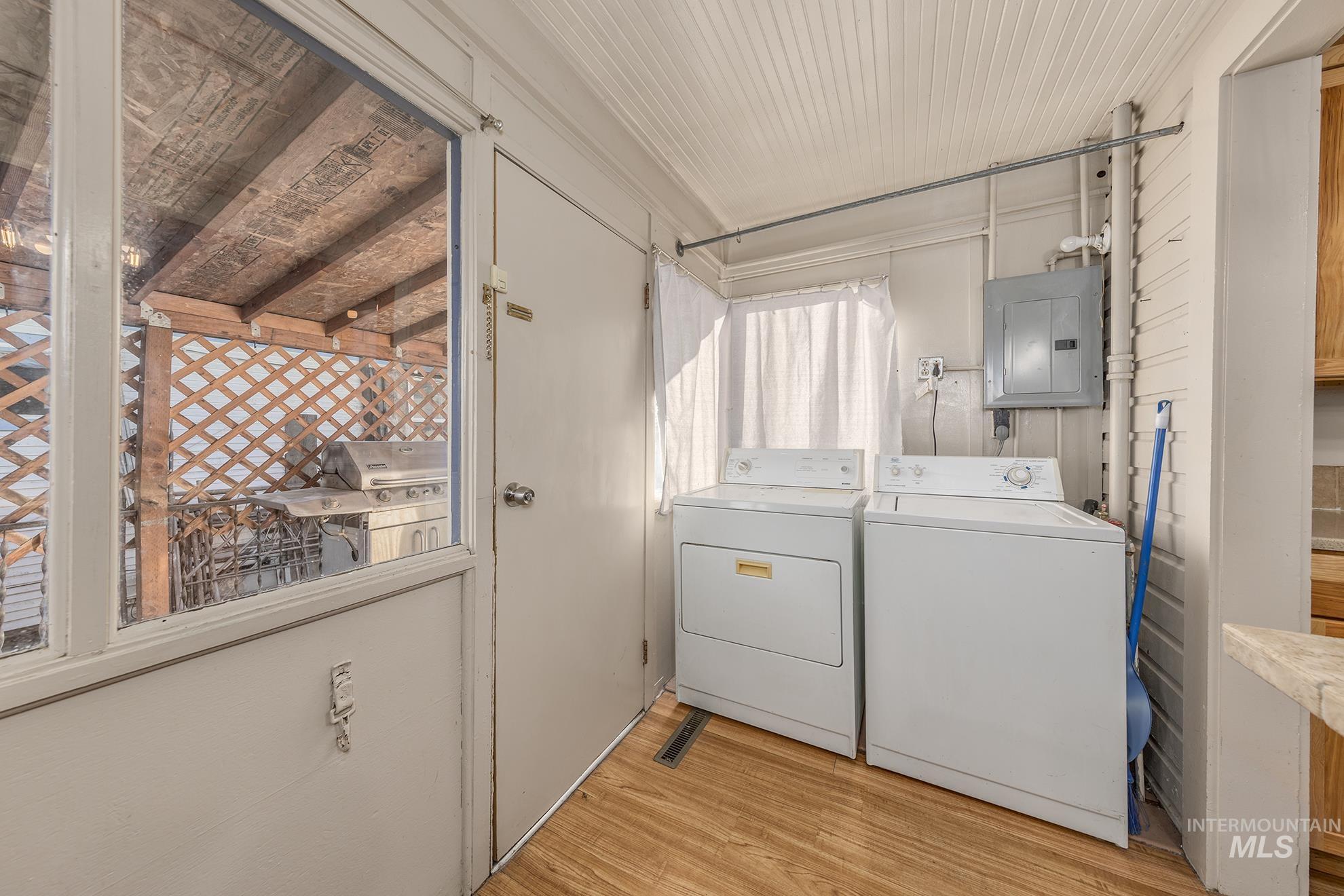Washroom featuring electric panel, washing machine and clothes dryer, and light wood-type flooring