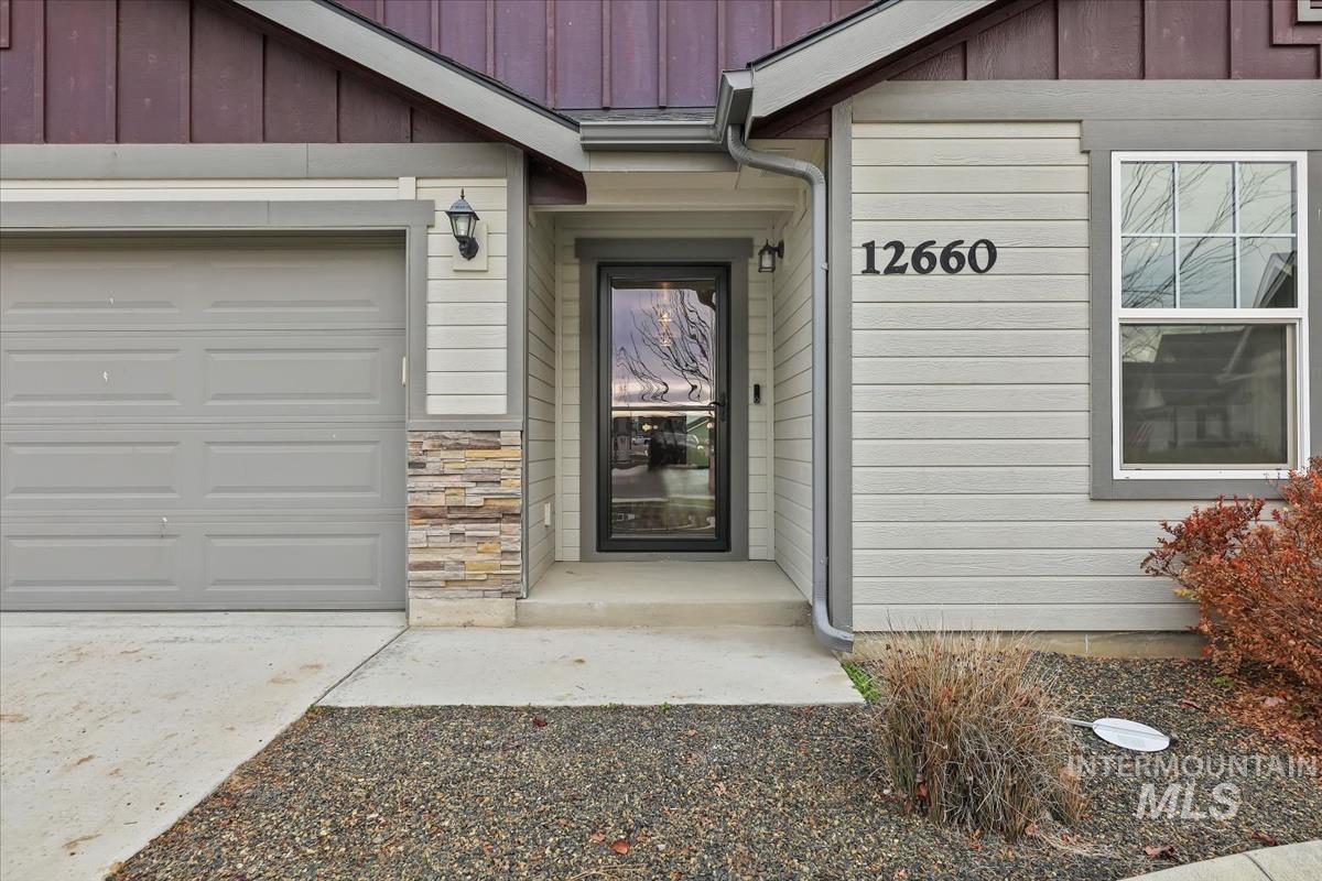 Doorway to property featuring board and batten siding, an attached garage, and stone siding