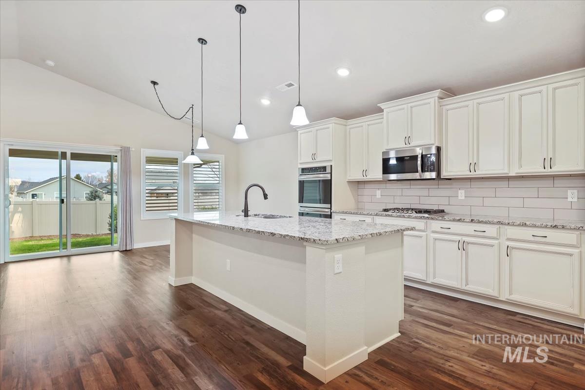 Kitchen featuring backsplash, hanging light fixtures, light stone countertops, a kitchen island with sink, and recessed lighting