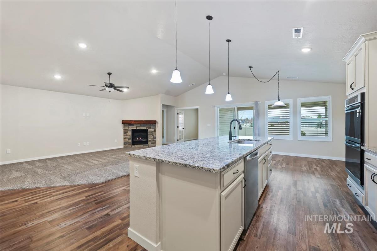 Kitchen with open floor plan, white cabinetry, a stone fireplace, light stone countertops, and a center island with sink