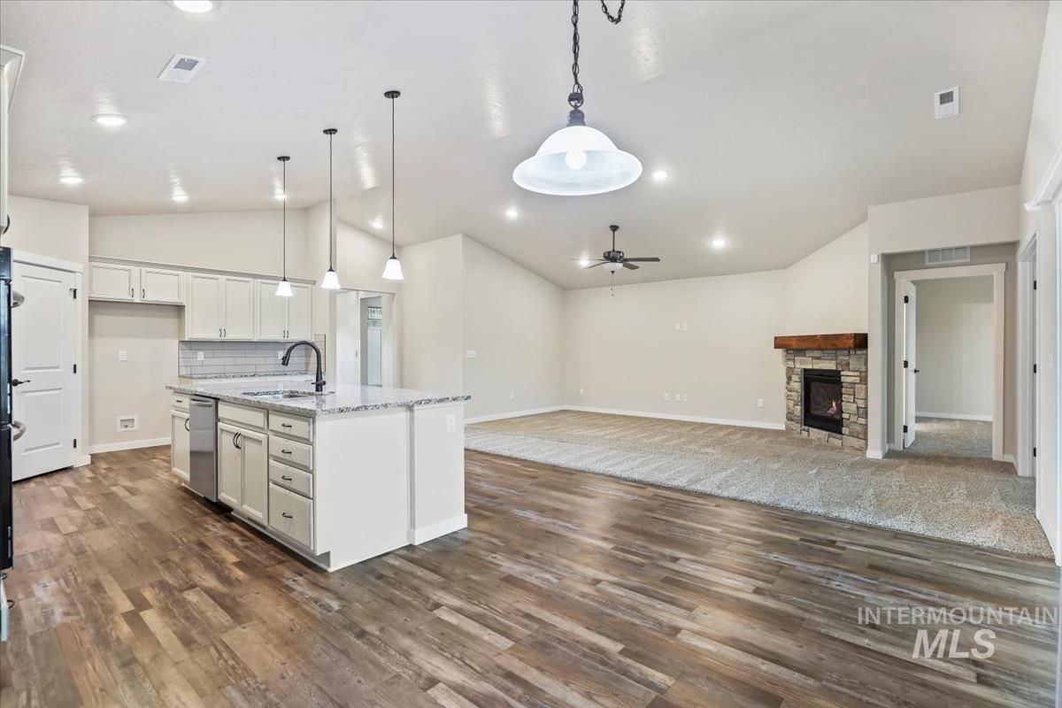 Kitchen featuring lofted ceiling, decorative light fixtures, open floor plan, a fireplace, and a kitchen island with sink