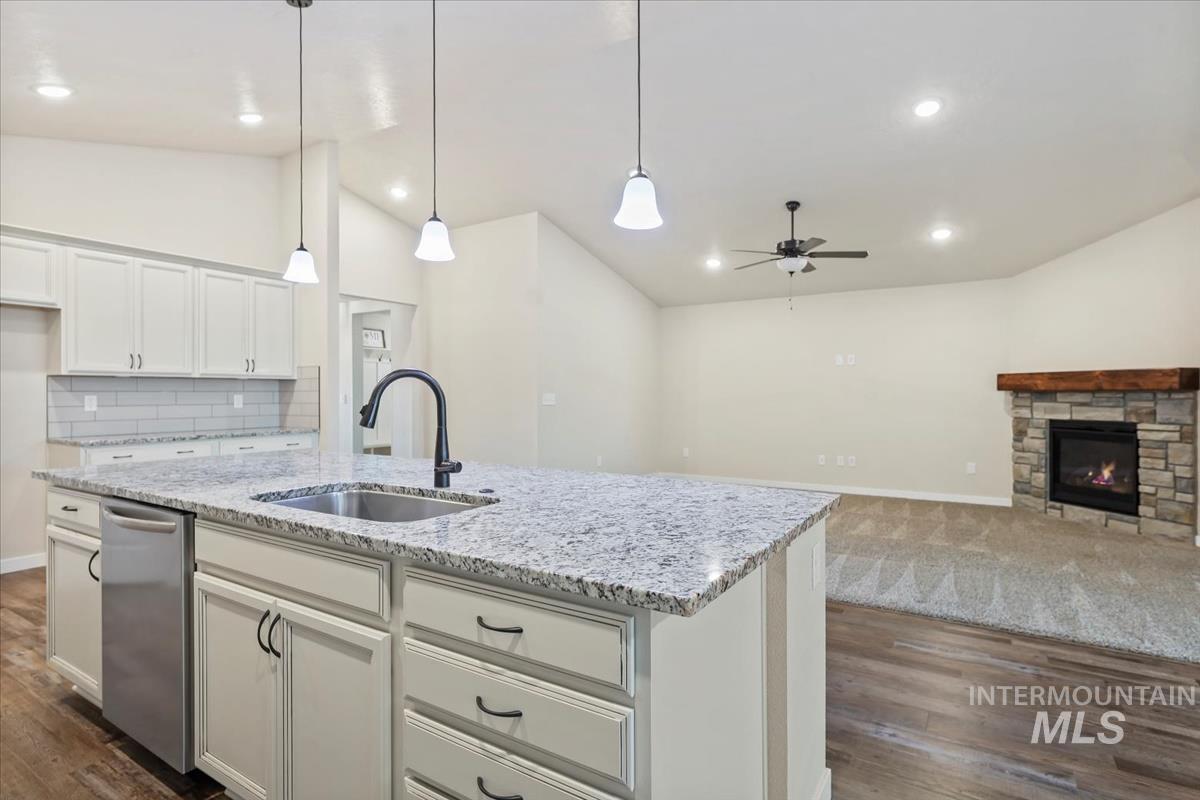 Kitchen featuring vaulted ceiling, decorative light fixtures, a stone fireplace, dark wood-style flooring, and white cabinetry