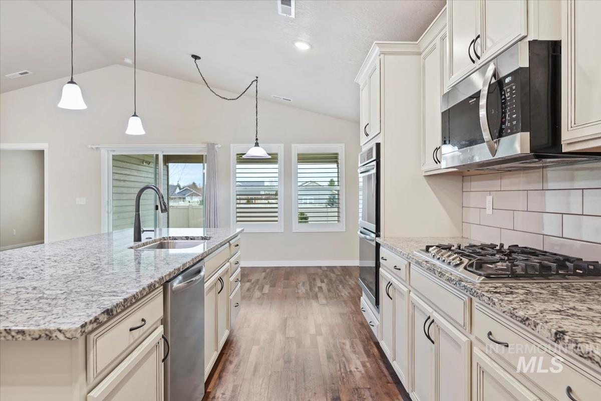 Kitchen with light stone countertops, pendant lighting, a kitchen island with sink, white cabinets, and lofted ceiling