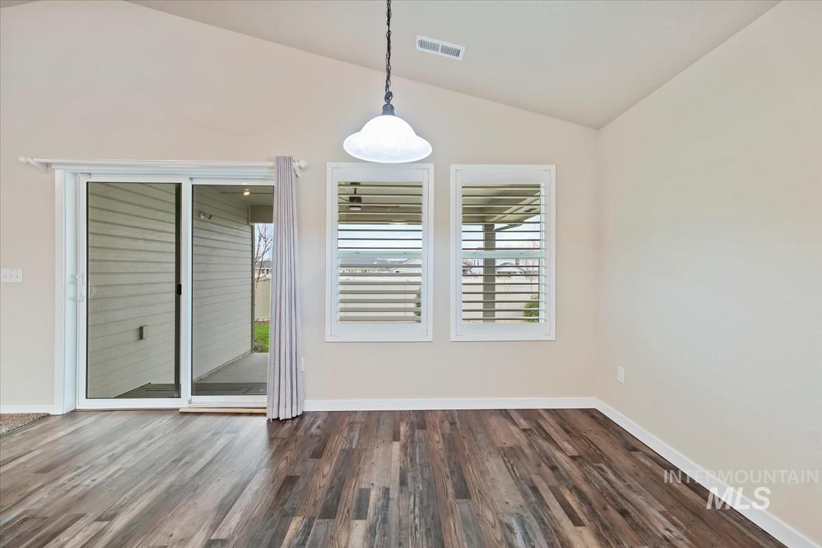 Unfurnished dining area featuring vaulted ceiling and dark wood-style flooring