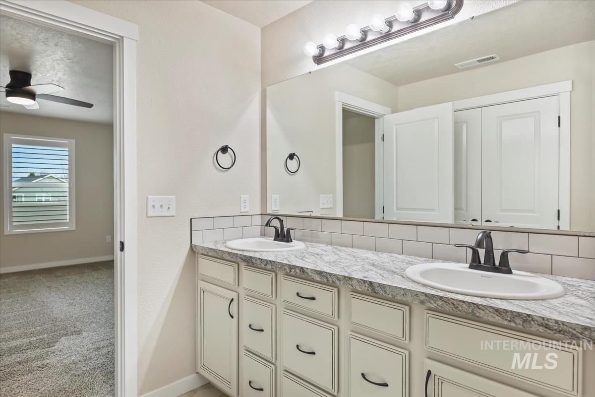Bathroom with tasteful backsplash, light carpet, double vanity, and a ceiling fan