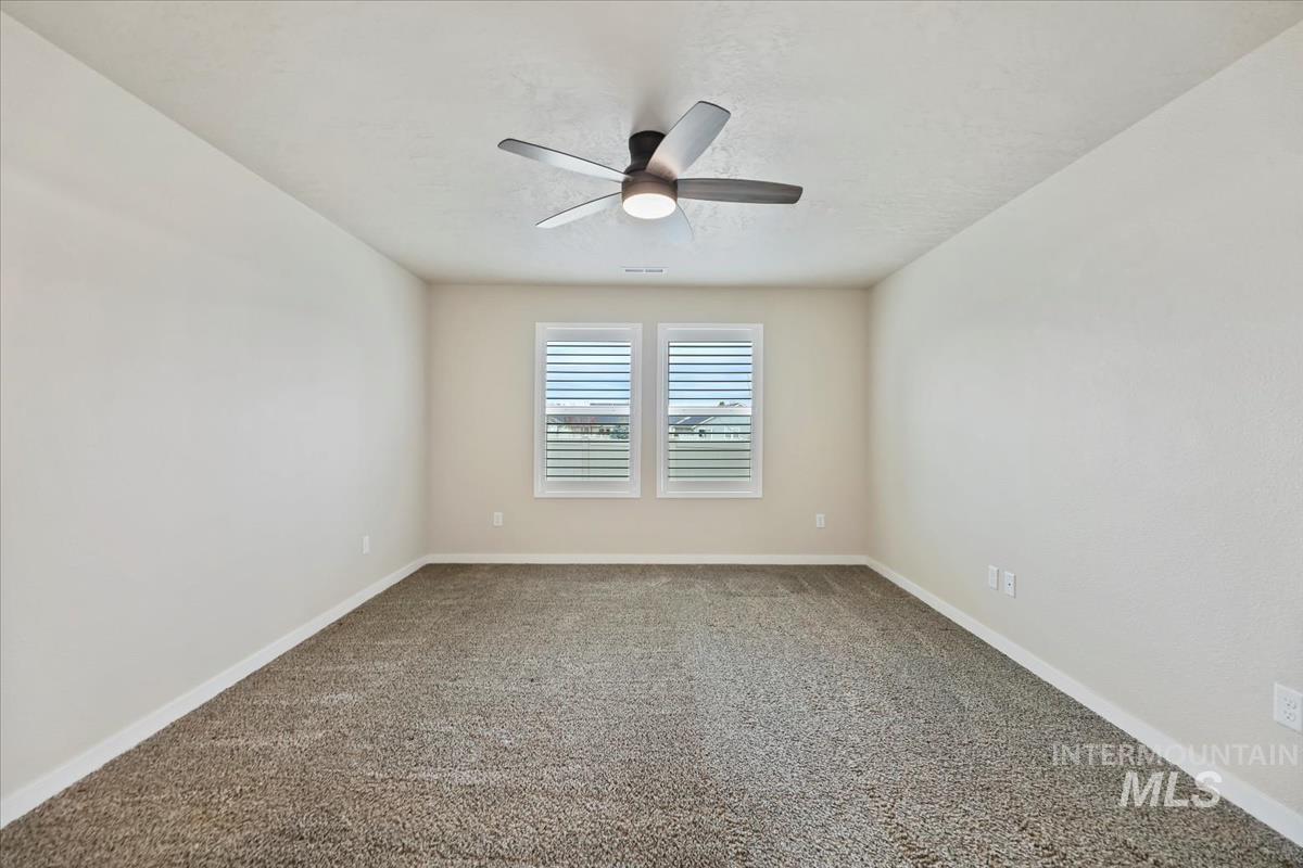 Carpeted empty room with baseboards and a ceiling fan
