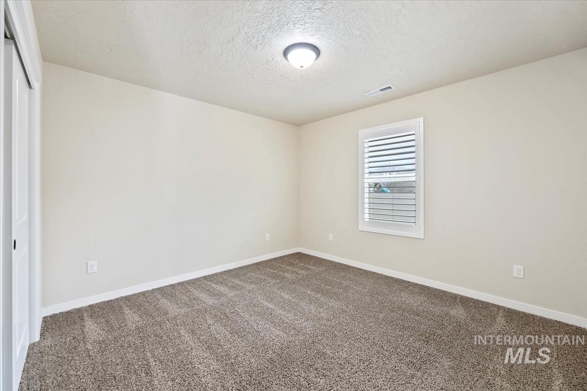 Carpeted spare room featuring a textured ceiling and baseboards