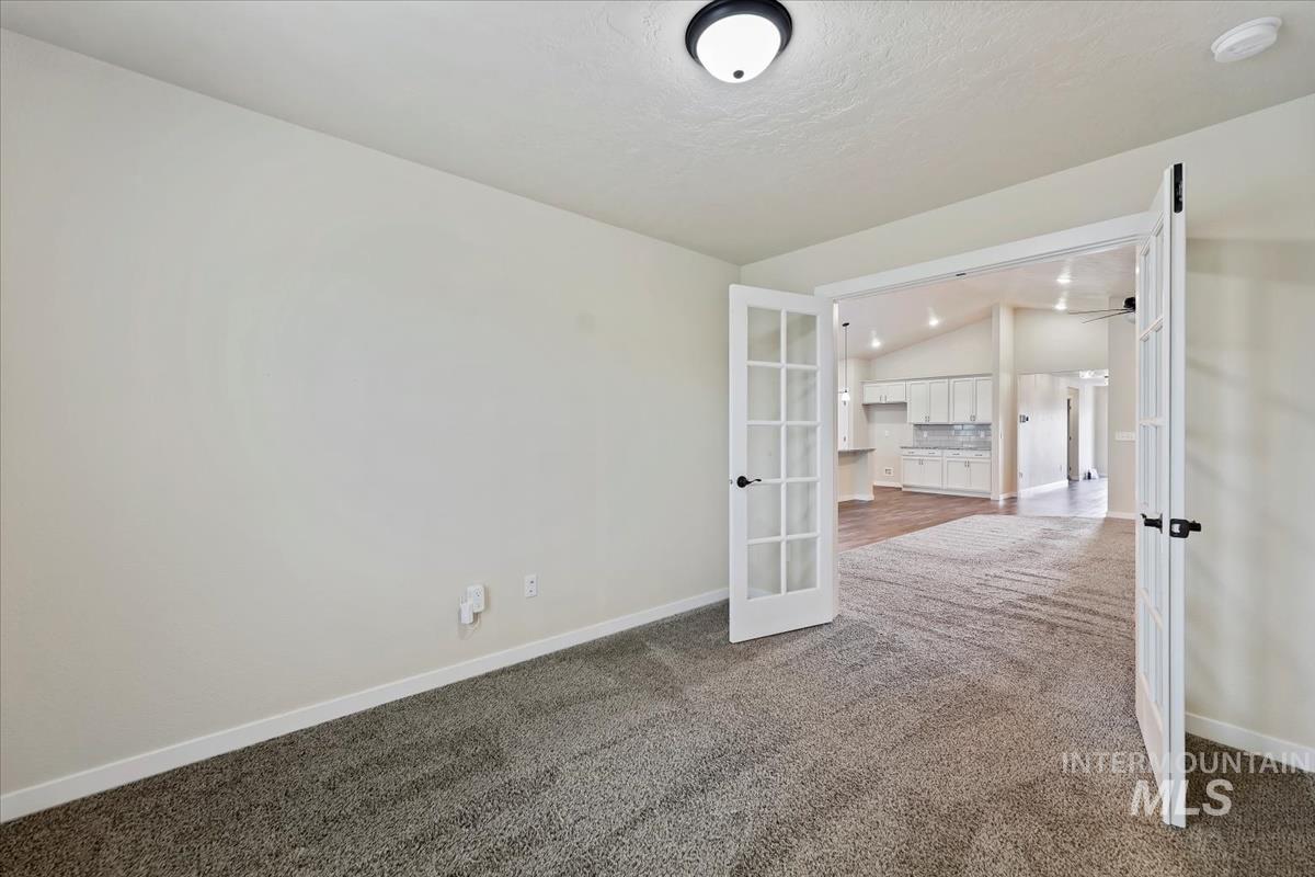 Empty room featuring lofted ceiling, dark colored carpet, and french doors