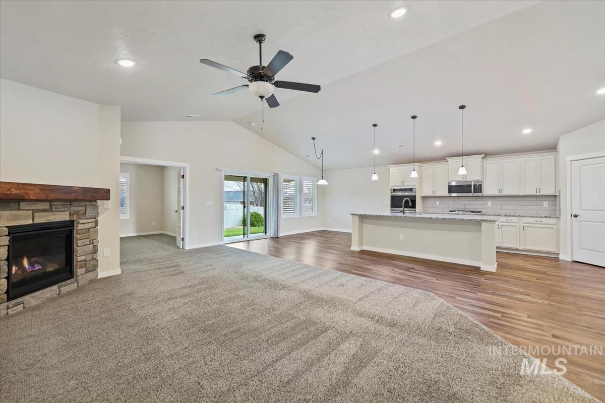 Unfurnished living room featuring lofted ceiling, a stone fireplace, ceiling fan, recessed lighting, and light wood-type flooring