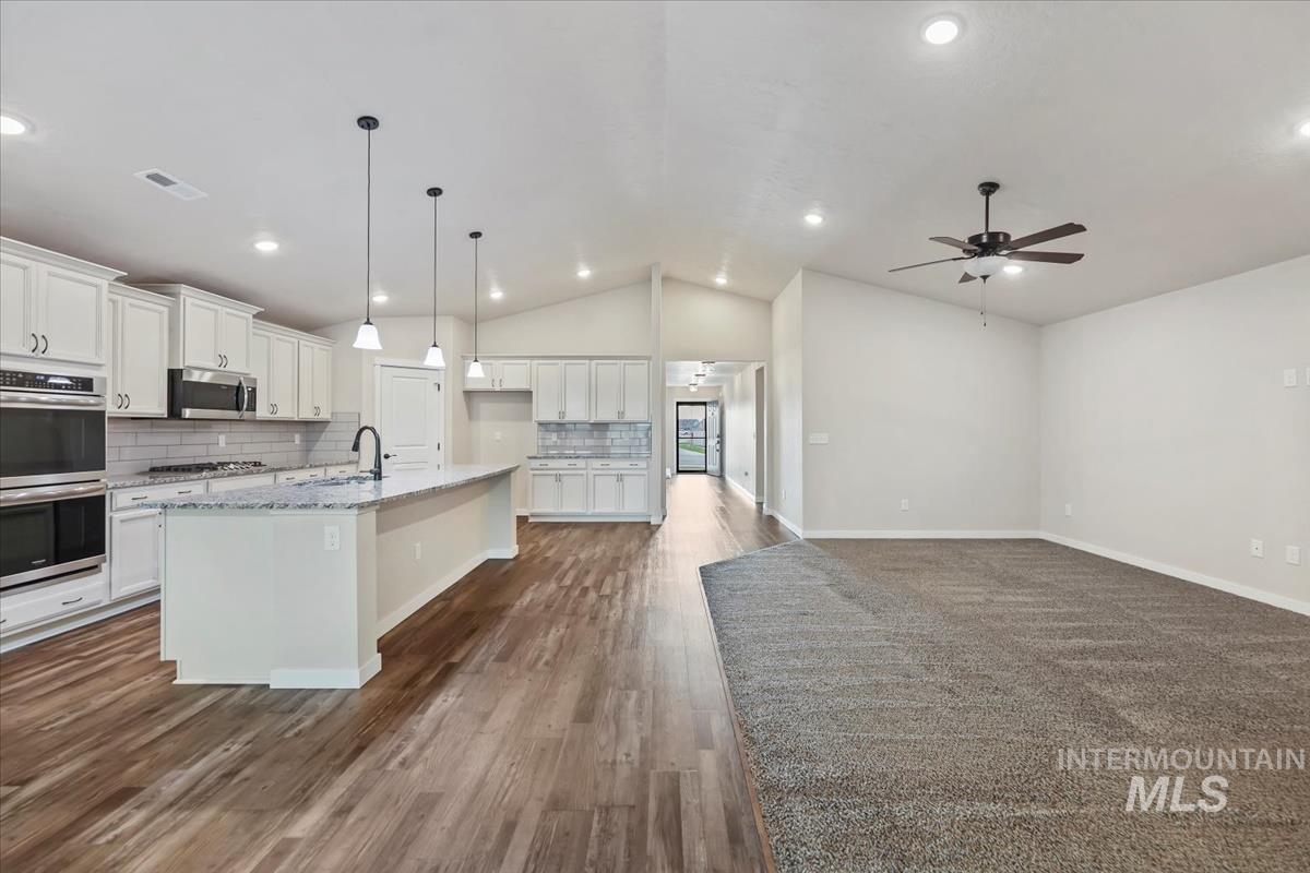Kitchen with stainless steel appliances, lofted ceiling, an island with sink, white cabinetry, and decorative backsplash