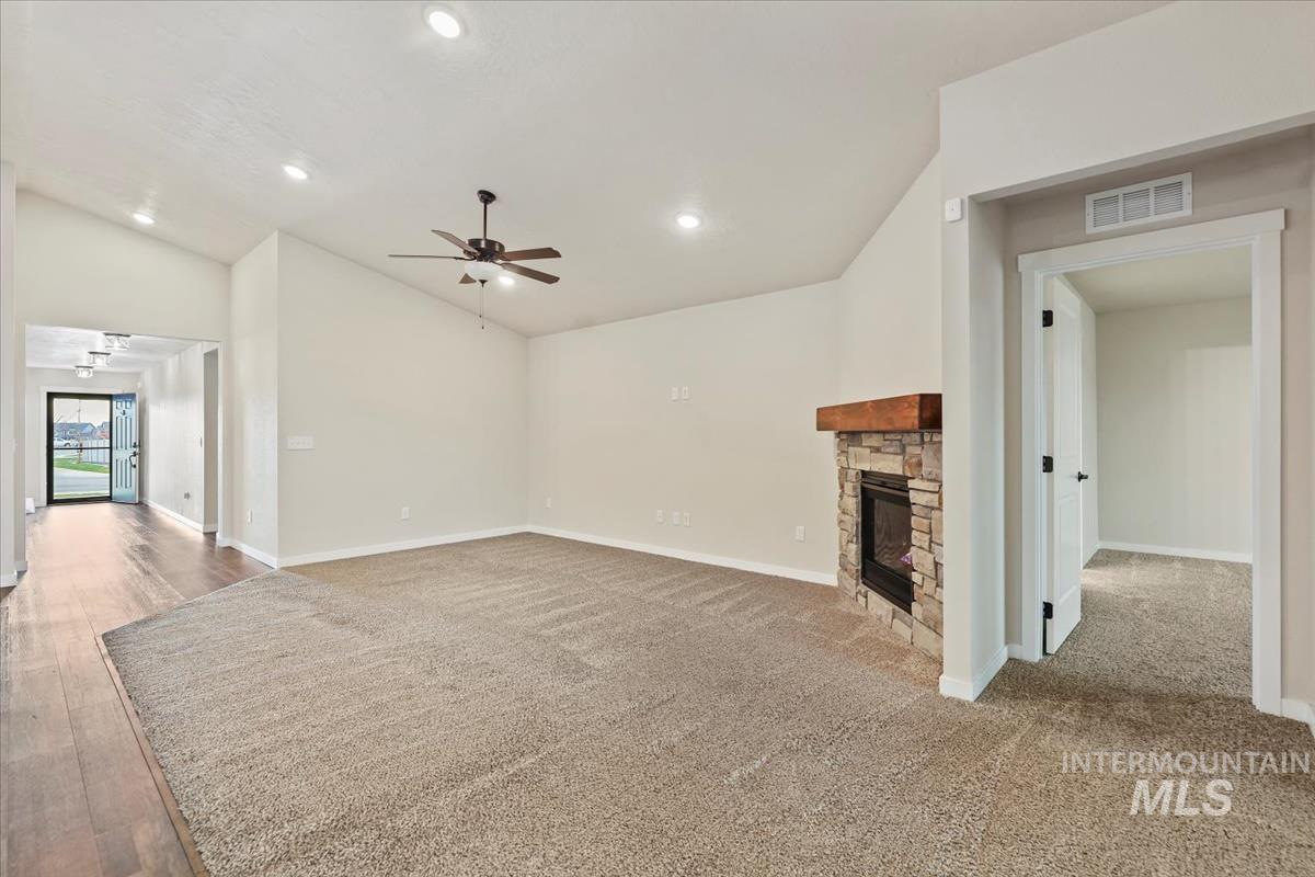 Unfurnished living room featuring a stone fireplace, recessed lighting, vaulted ceiling, and a ceiling fan