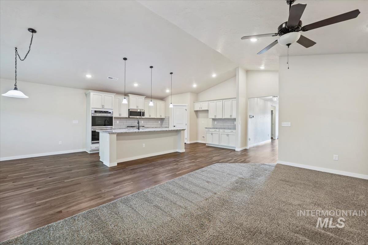 Kitchen featuring backsplash, vaulted ceiling, white cabinets, open floor plan, and a center island with sink