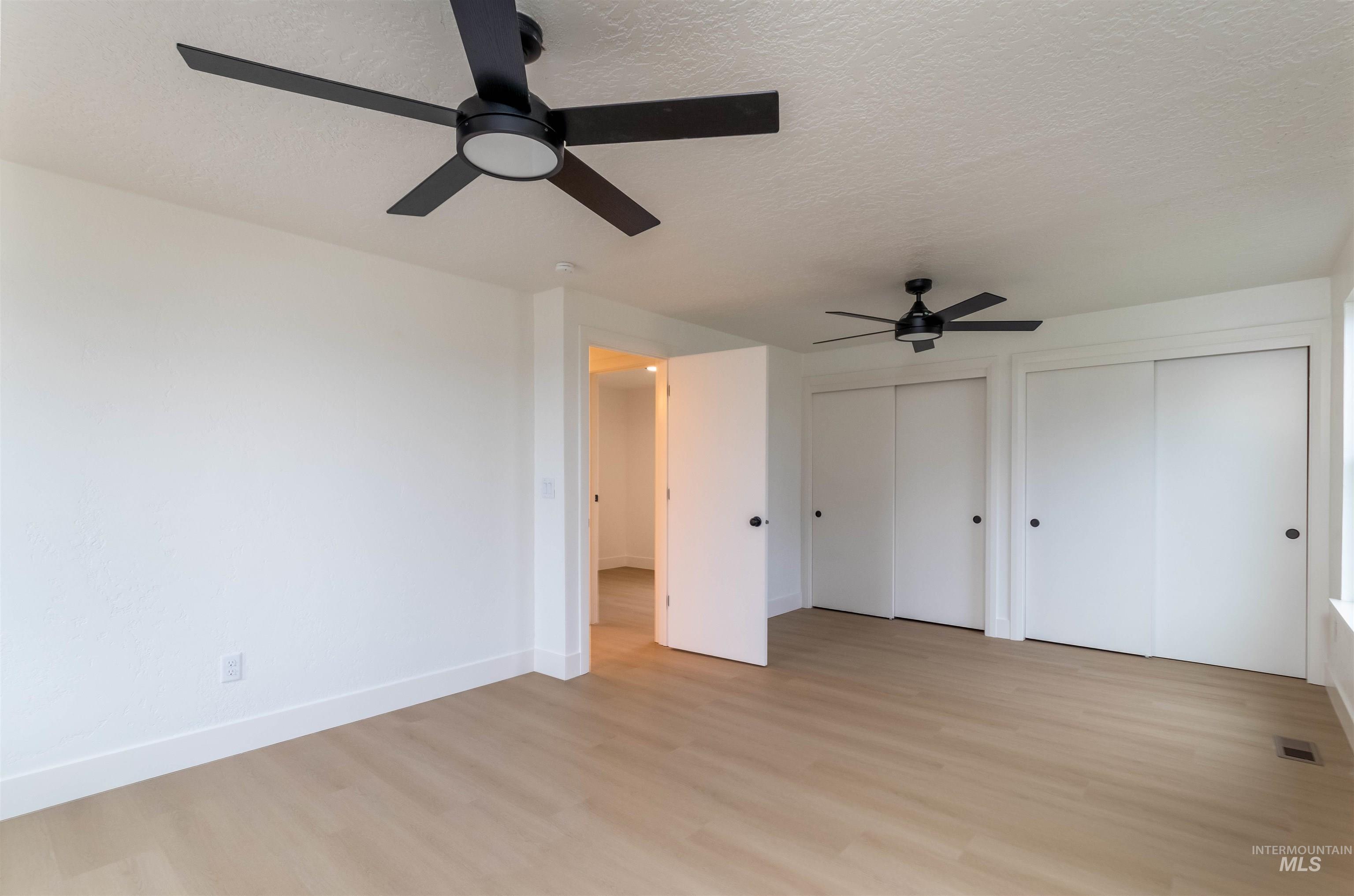 Unfurnished bedroom with two closets, light wood-style floors, a ceiling fan, and a textured ceiling