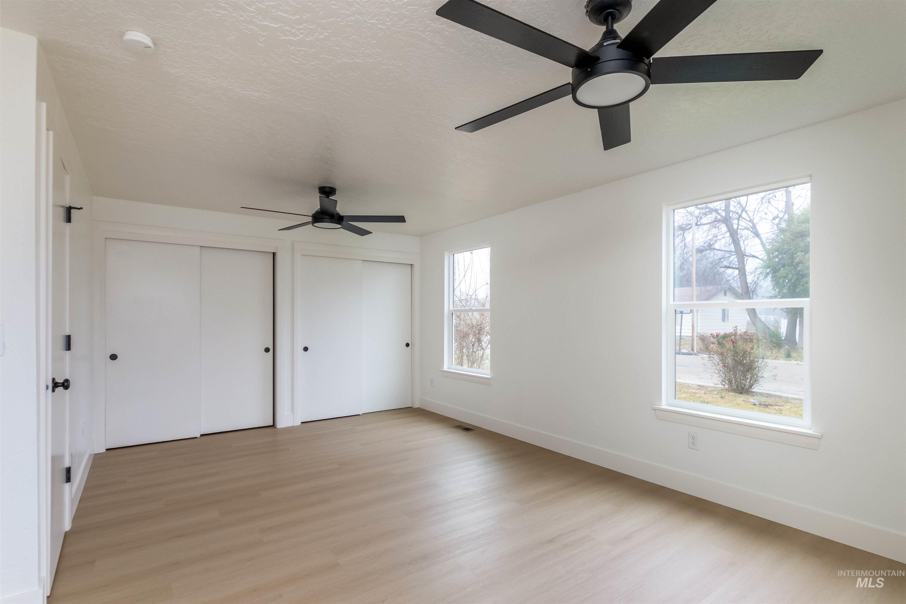 Unfurnished bedroom with two closets, light wood-type flooring, ceiling fan, and a textured ceiling