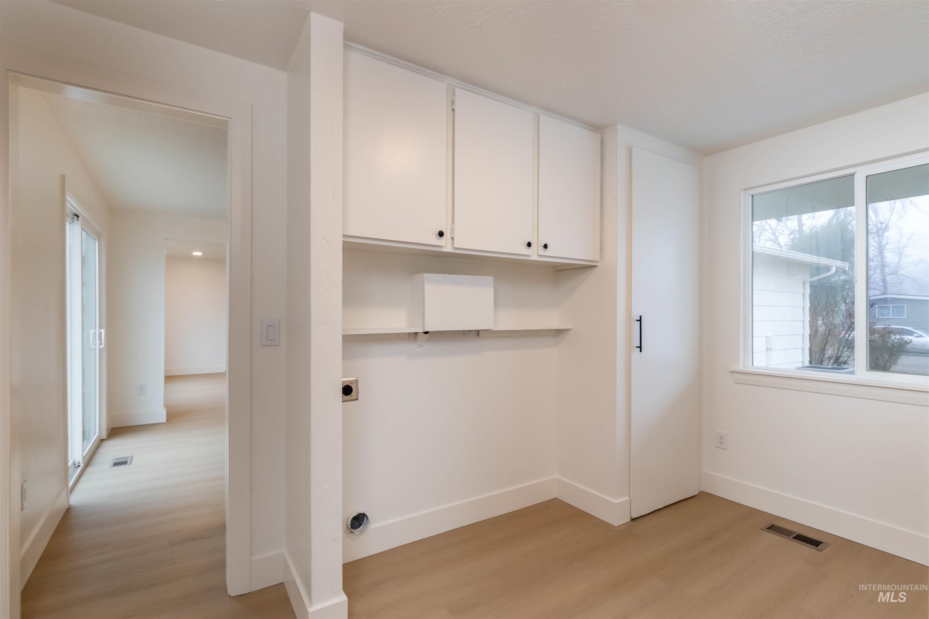 Laundry room with light wood-style flooring, hookup for an electric dryer, and cabinet space