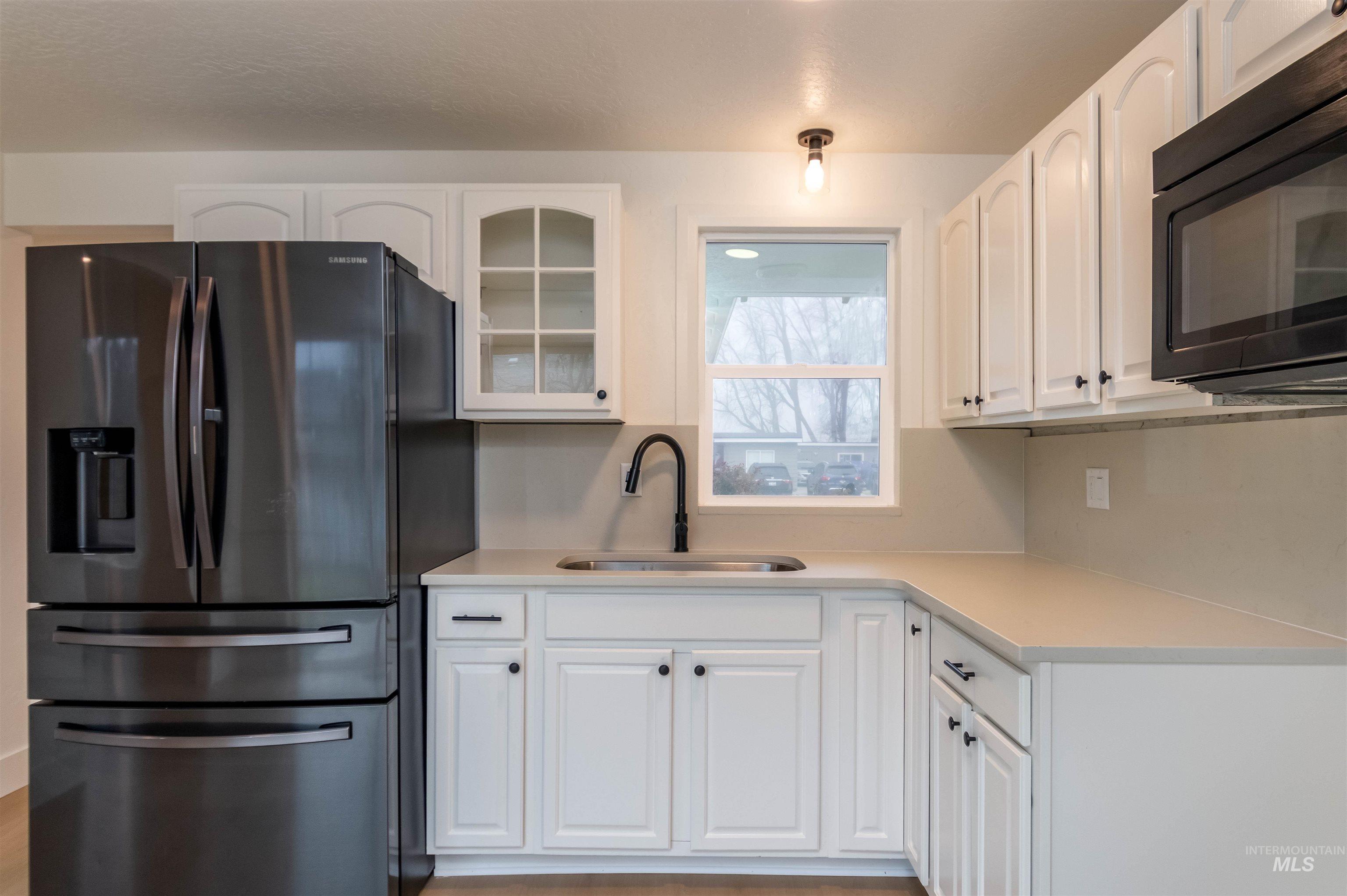Kitchen with refrigerator with ice dispenser, black microwave, white cabinets, and glass insert cabinets