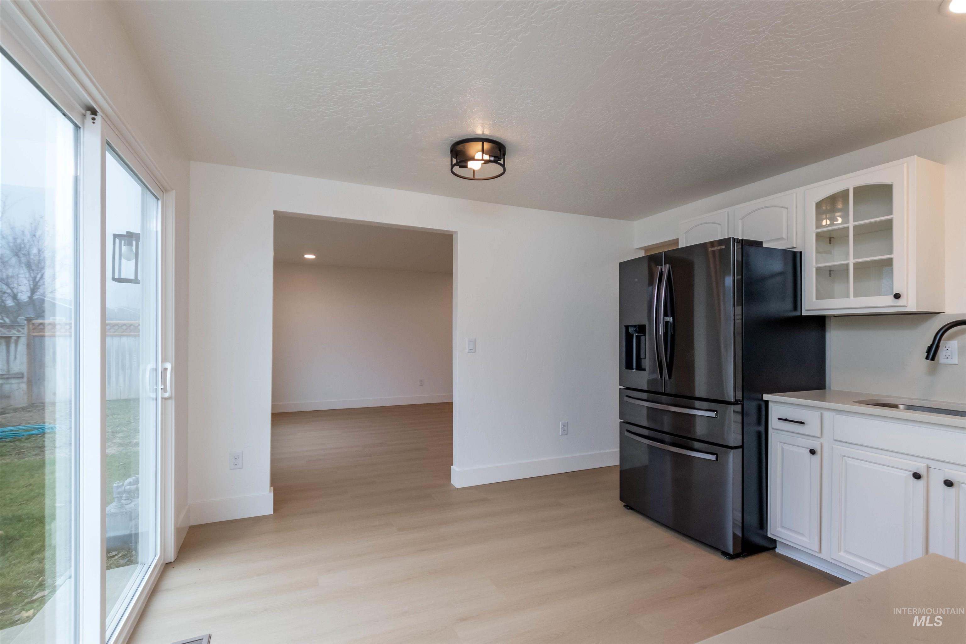 Kitchen with glass insert cabinets, refrigerator with ice dispenser, white cabinets, a textured ceiling, and light wood-type flooring