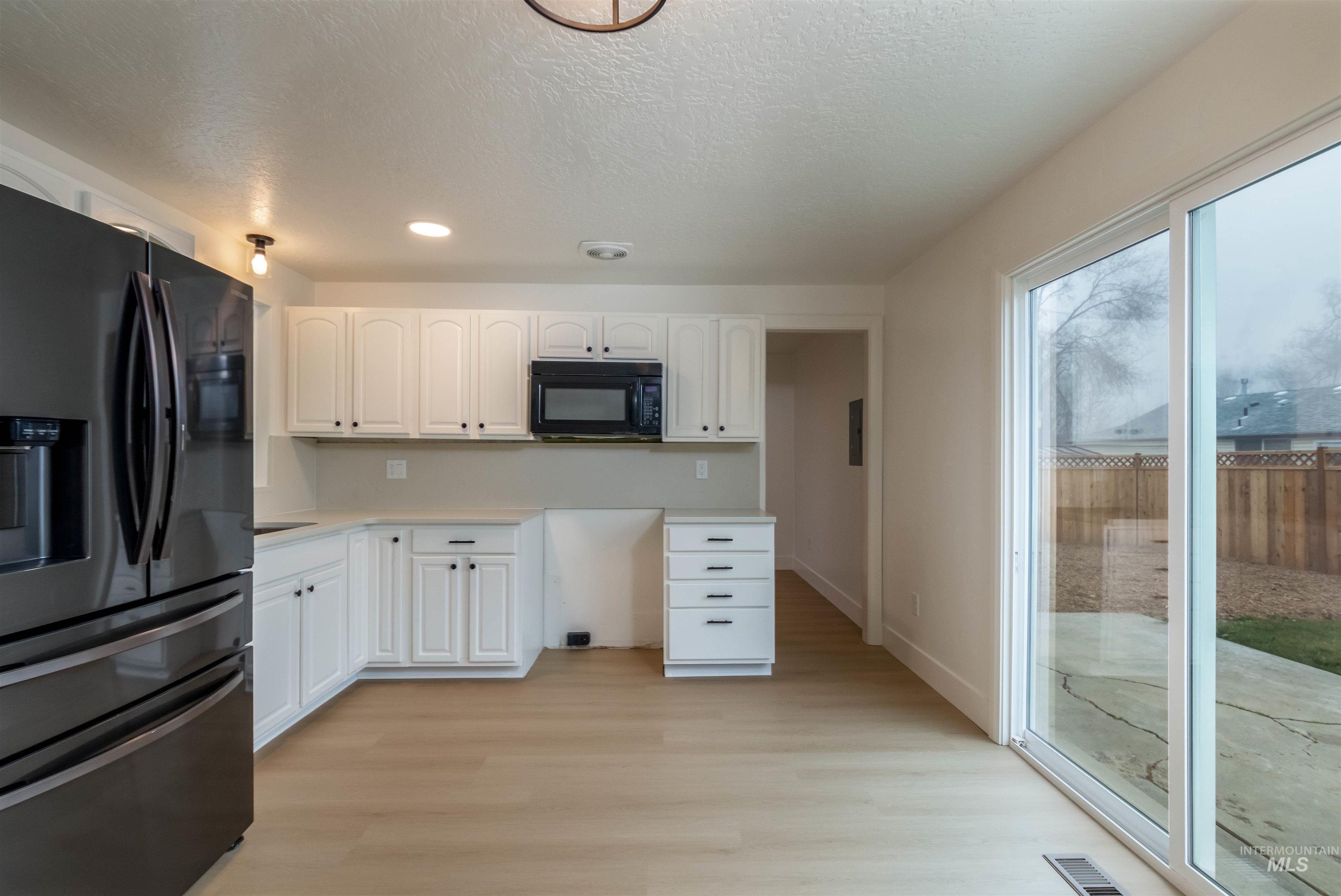 Kitchen featuring black appliances, white cabinets, light countertops, light wood-style flooring, and a textured ceiling