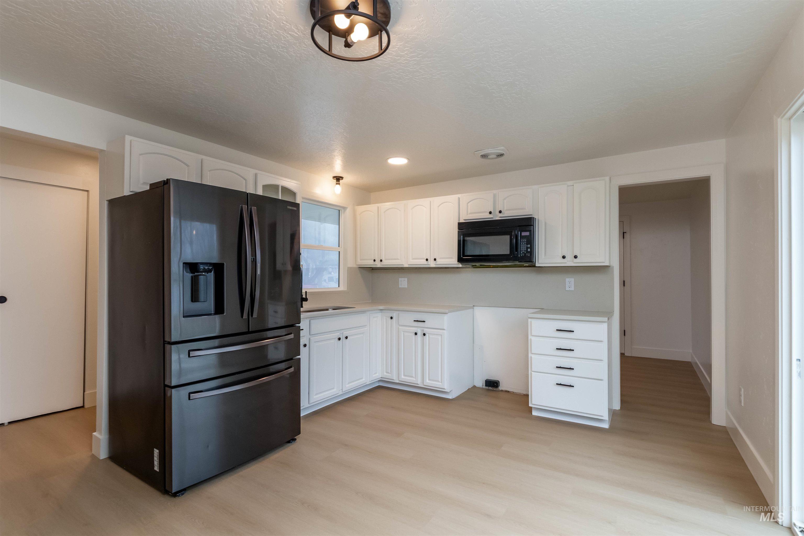 Kitchen with stainless steel fridge with ice dispenser, white cabinetry, light countertops, black microwave, and light wood-style flooring
