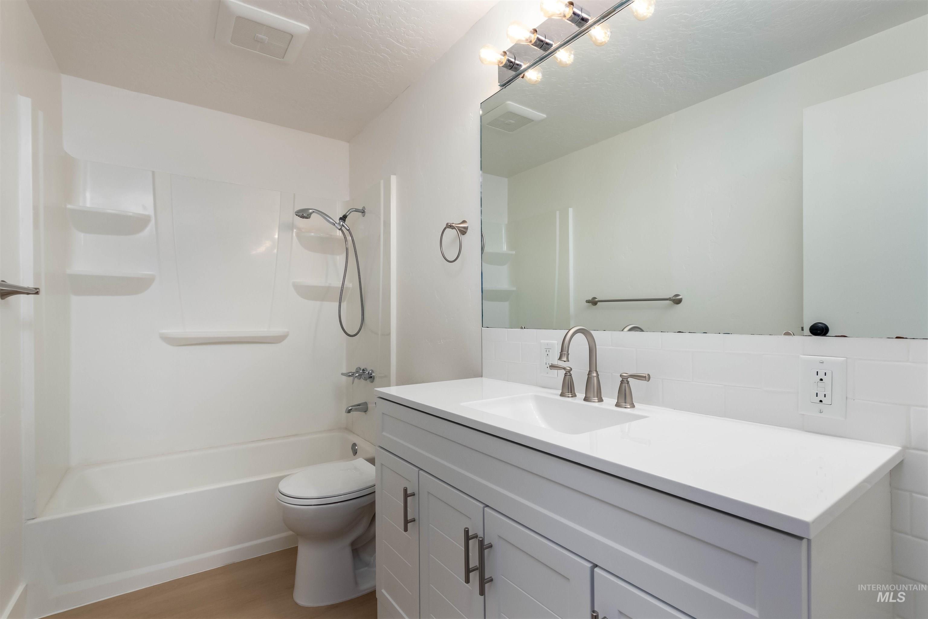 Full bathroom with vanity, shower / tub combination, light wood finished floors, and a textured ceiling