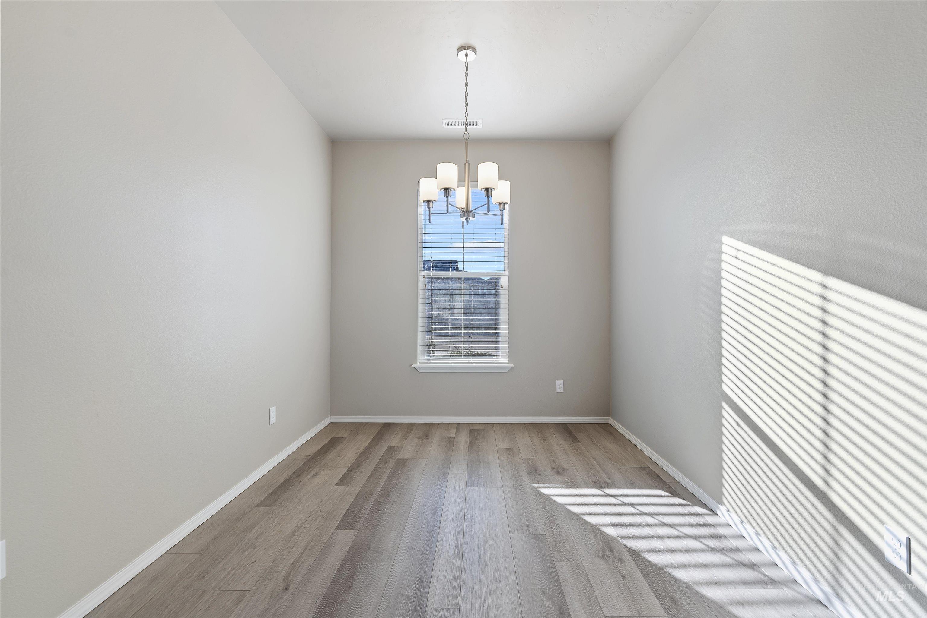 Empty room with light wood finished floors and a chandelier