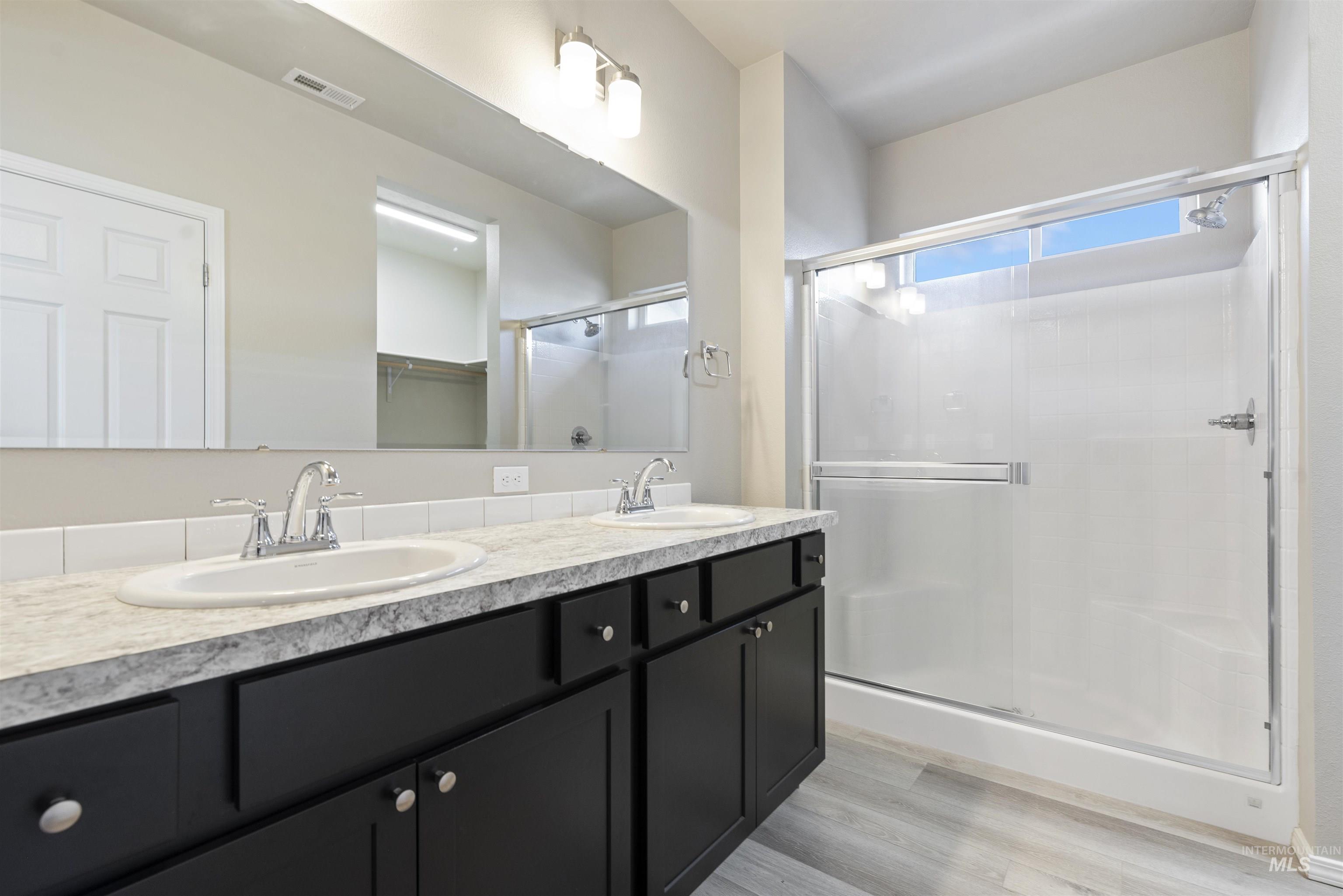 Full bathroom featuring double vanity, a stall shower, a spacious closet, and light wood-style flooring
