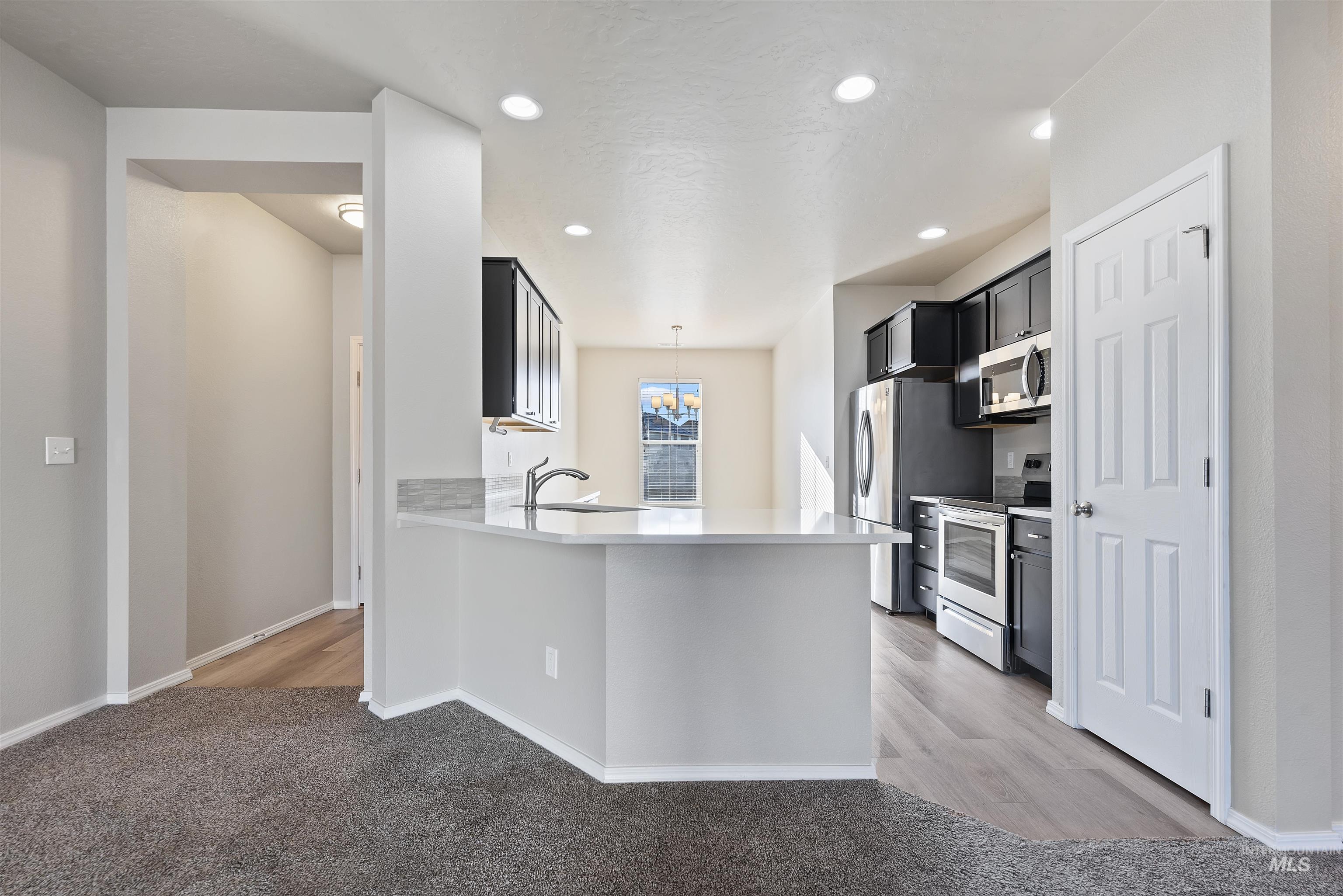 Kitchen with stainless steel appliances, dark cabinetry, decorative light fixtures, a peninsula, and recessed lighting