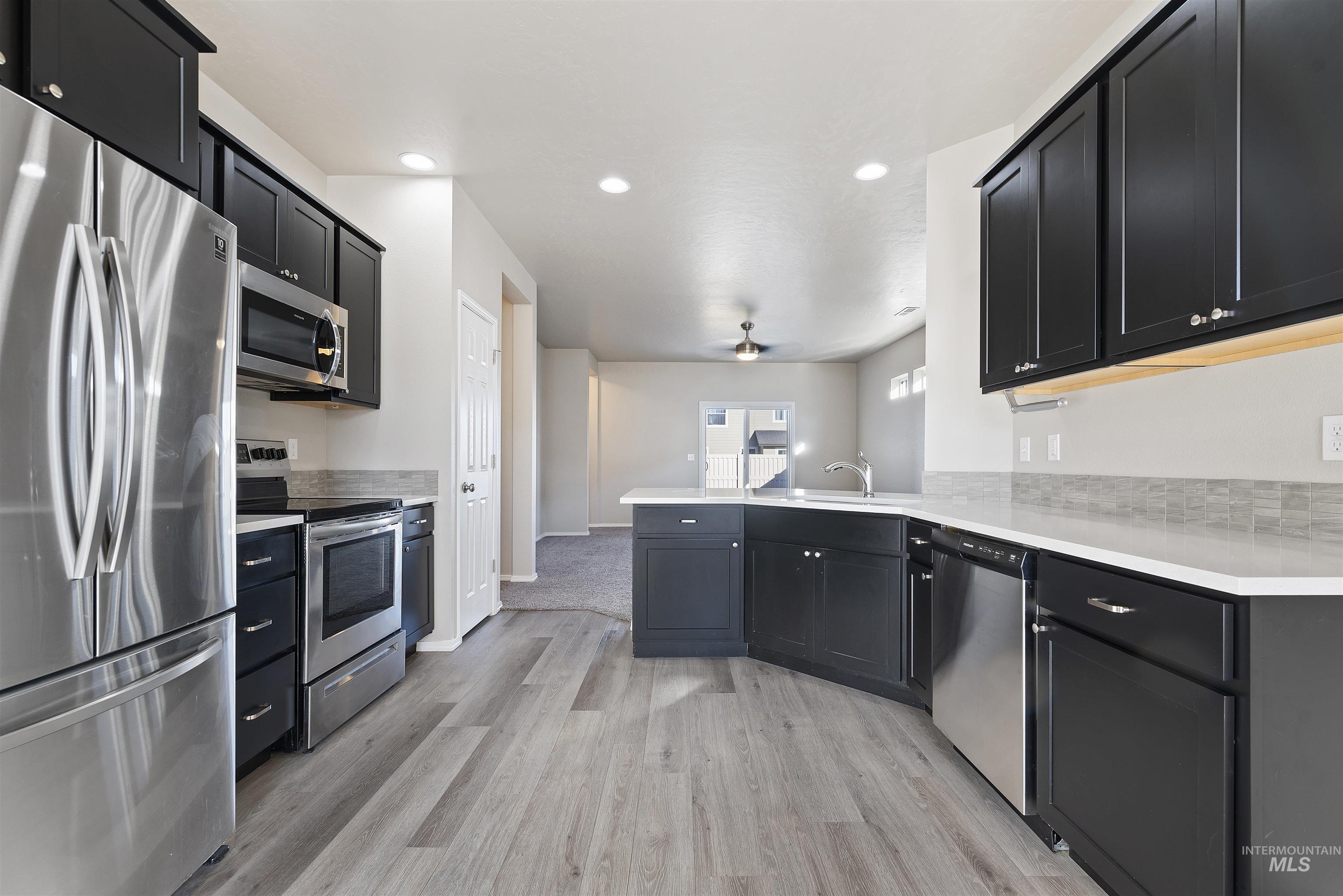 Kitchen featuring dark cabinets, appliances with stainless steel finishes, a peninsula, light wood-style flooring, and recessed lighting