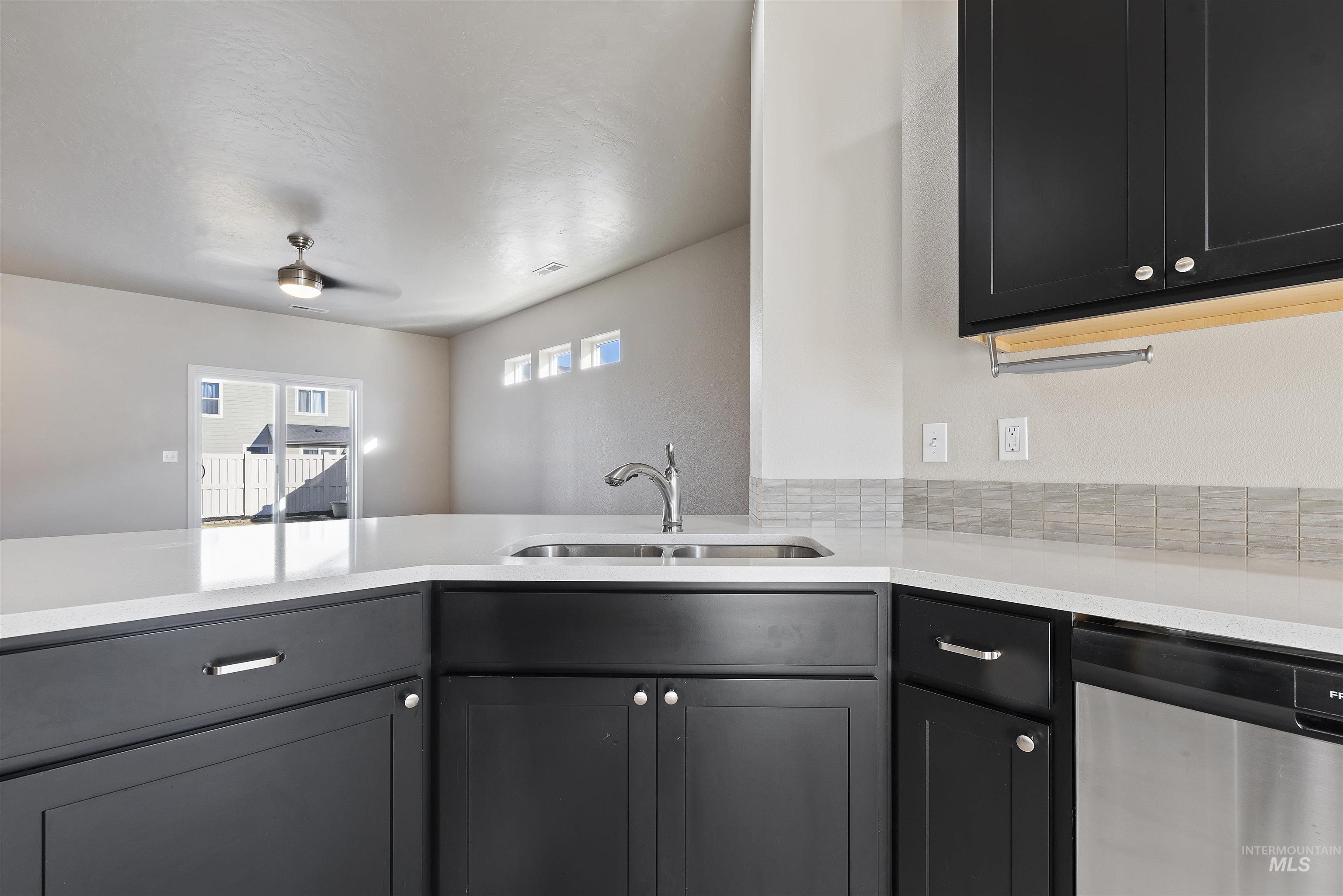 Kitchen featuring dishwasher, light stone countertops, a ceiling fan, and dark cabinetry