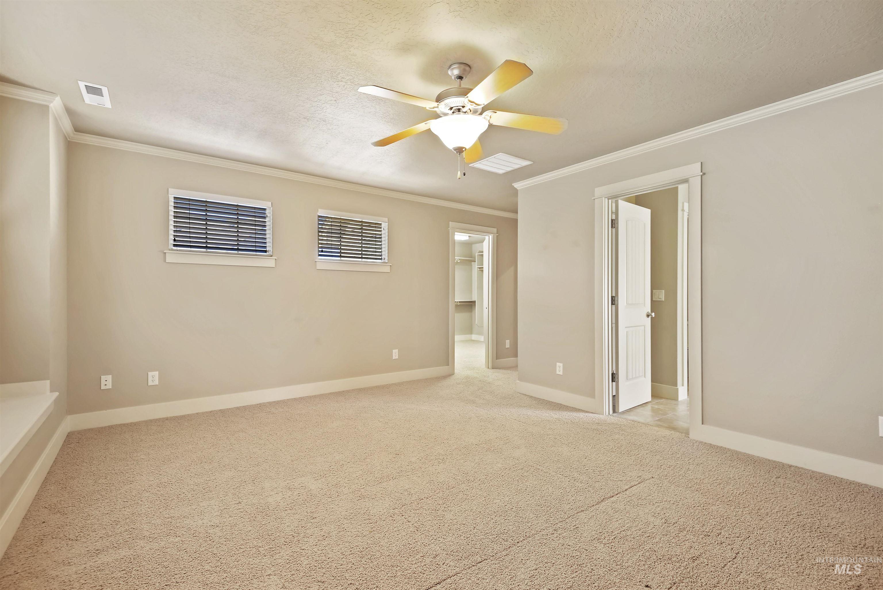 Unfurnished bedroom featuring ornamental molding, a textured ceiling, light colored carpet, and ceiling fan