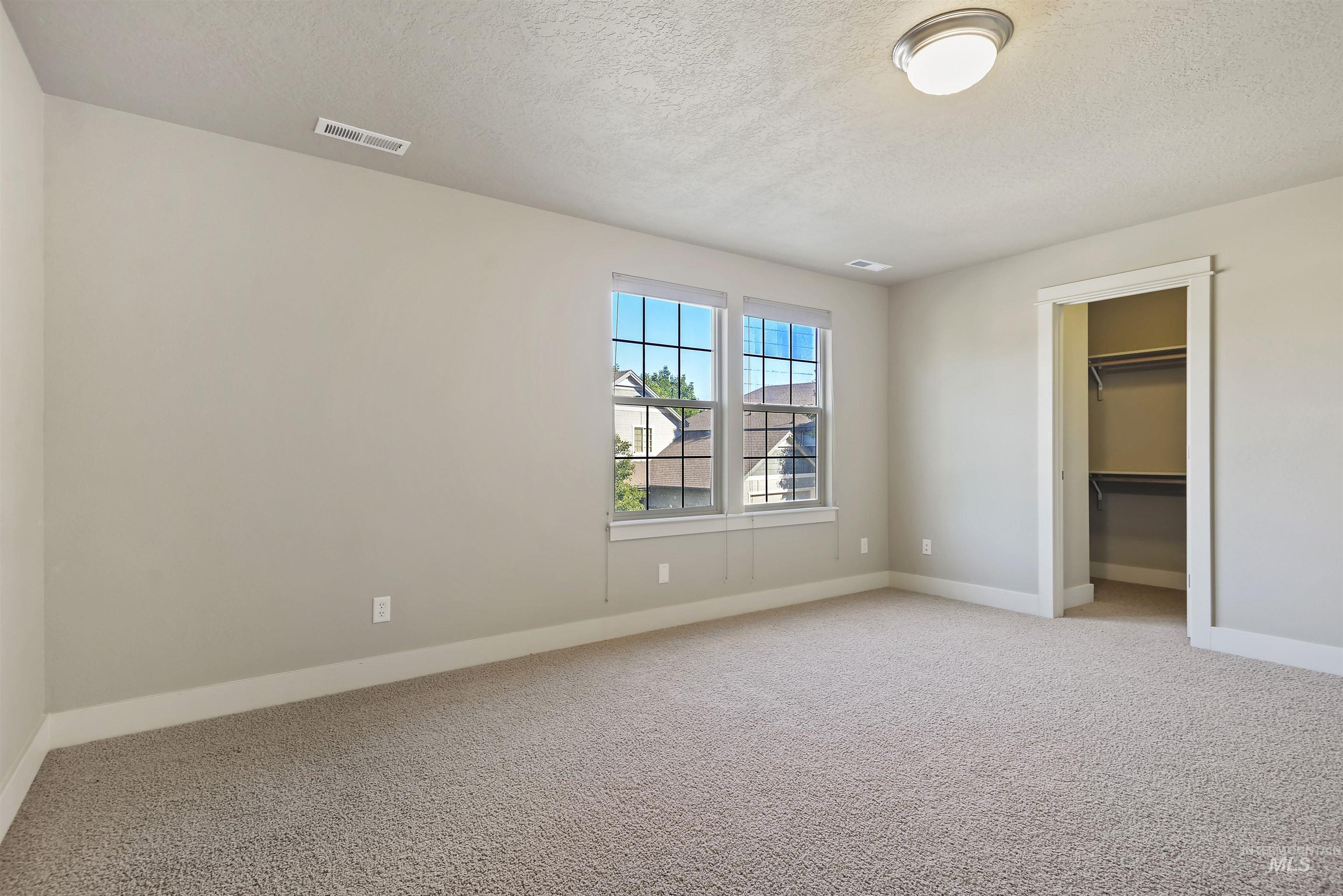 Unfurnished bedroom with light colored carpet, a walk in closet, and a textured ceiling