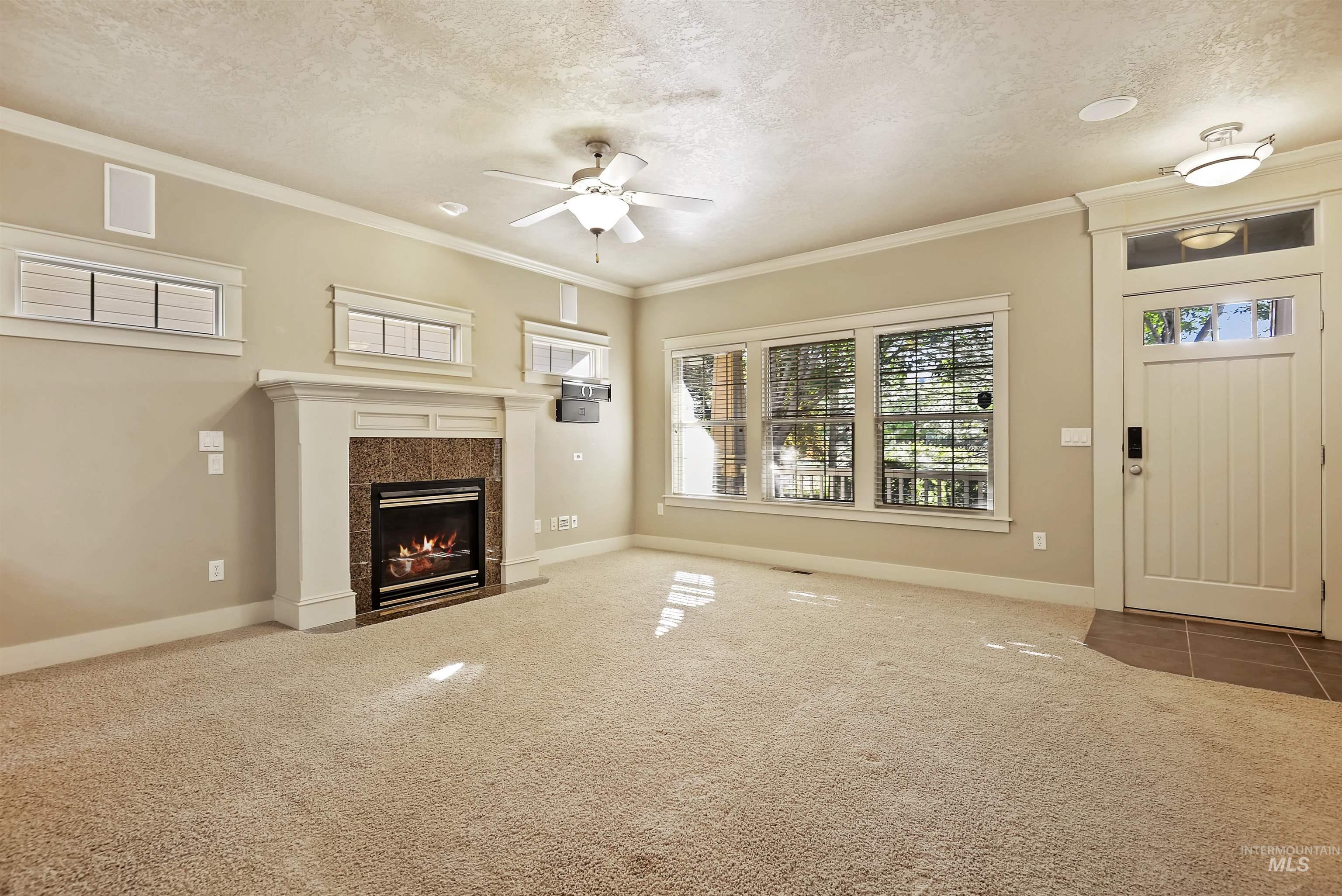 Unfurnished living room with a textured ceiling, carpet, ornamental molding, a fireplace, and a ceiling fan