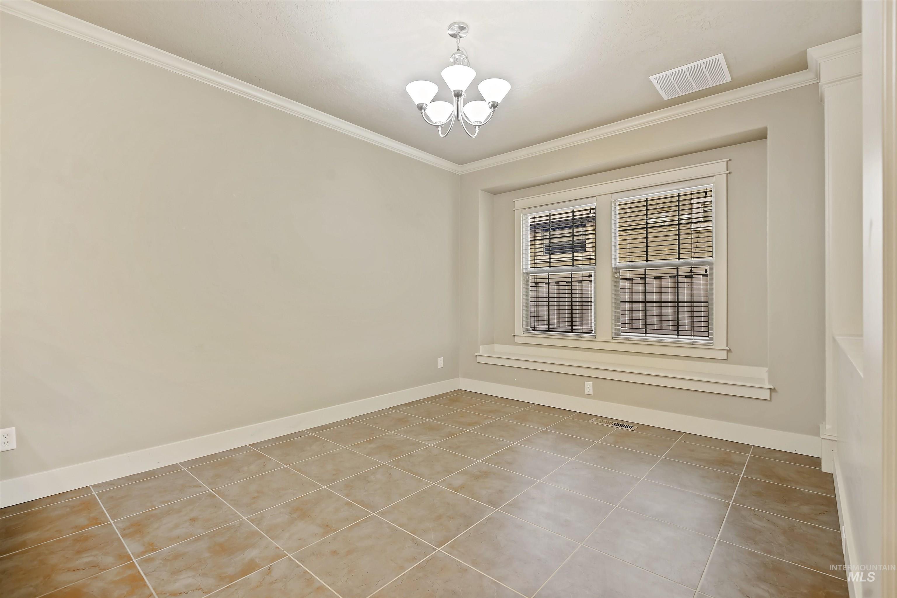 Empty room featuring ornamental molding, a chandelier, and light tile patterned floors