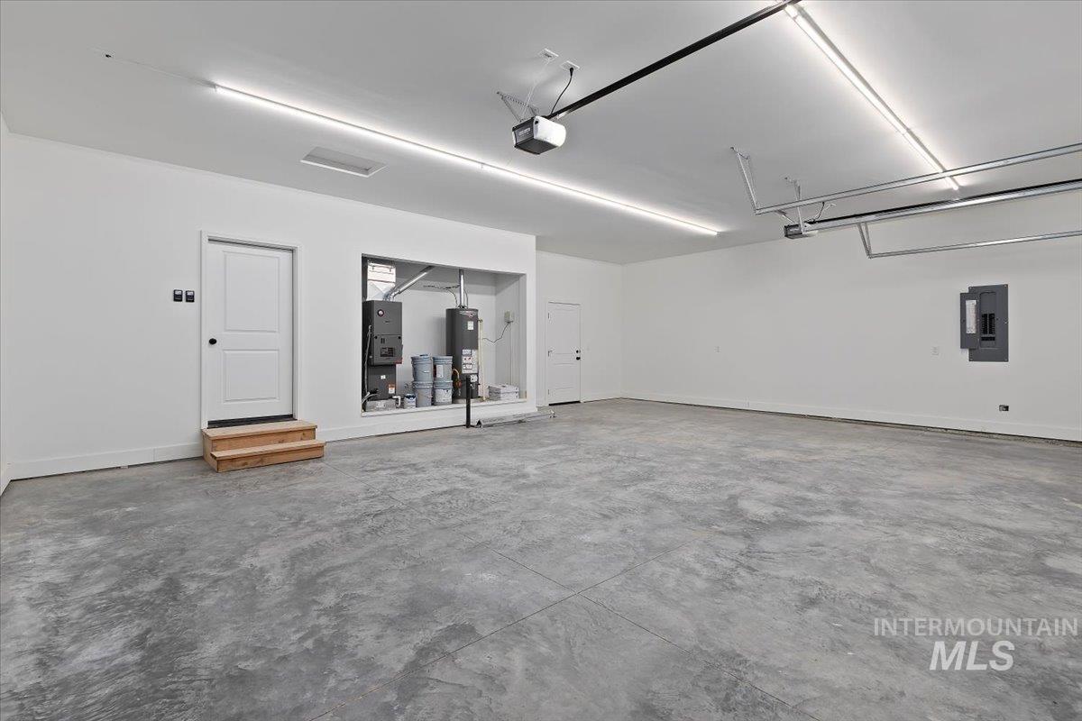 Garage featuring electric panel, water heater, and heating unit