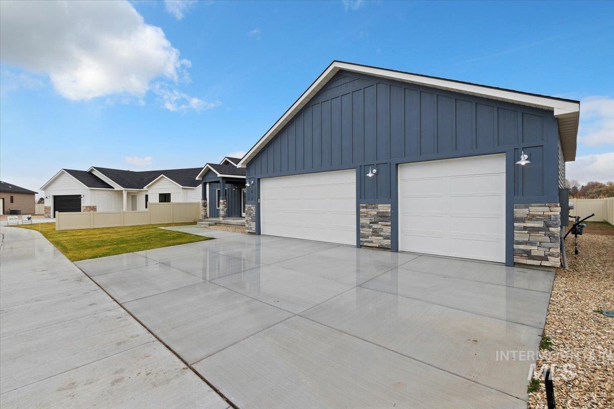 View of front of property featuring board and batten siding, stone siding, a garage, and driveway