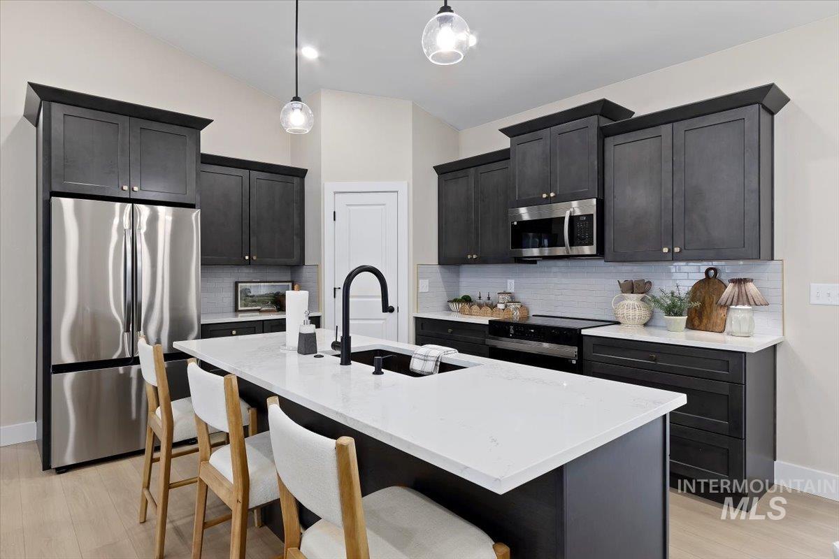Kitchen featuring stainless steel appliances, light stone counters, a kitchen breakfast bar, a center island with sink, and pendant lighting